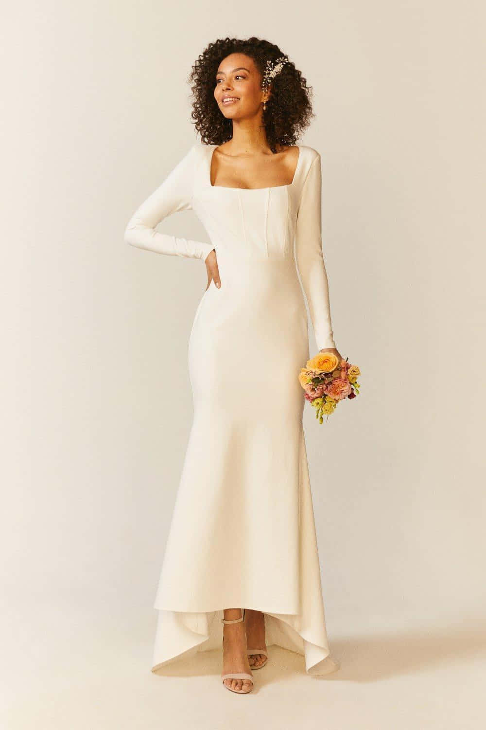 White Dress 桌布 壁紙 — 一位光彩照人的女士身穿優雅的象牙色美人魚婚紗，在柔和的純色背景下手持鮮豔的花束。