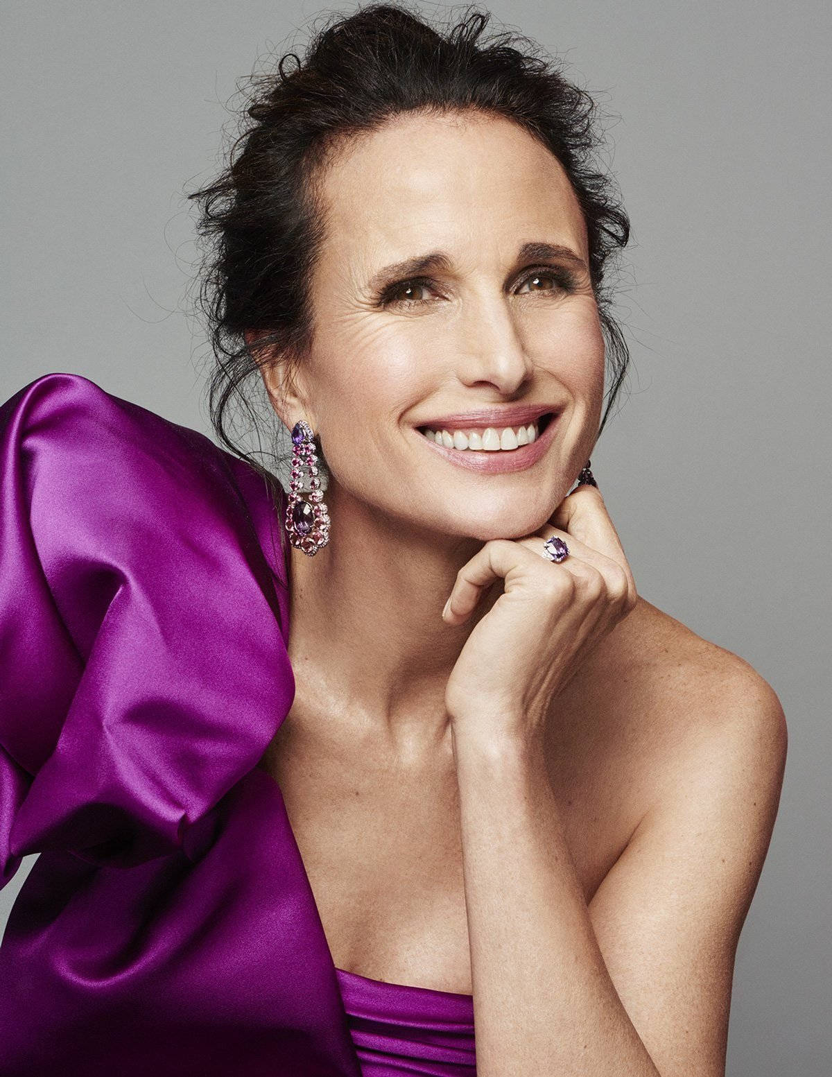 andie macdowell 桌布 壁紙 — 一位光彩照人的女士身穿鮮豔的紫色緞面禮服，微笑著將下巴擱在戴有閃亮珠寶的手上。