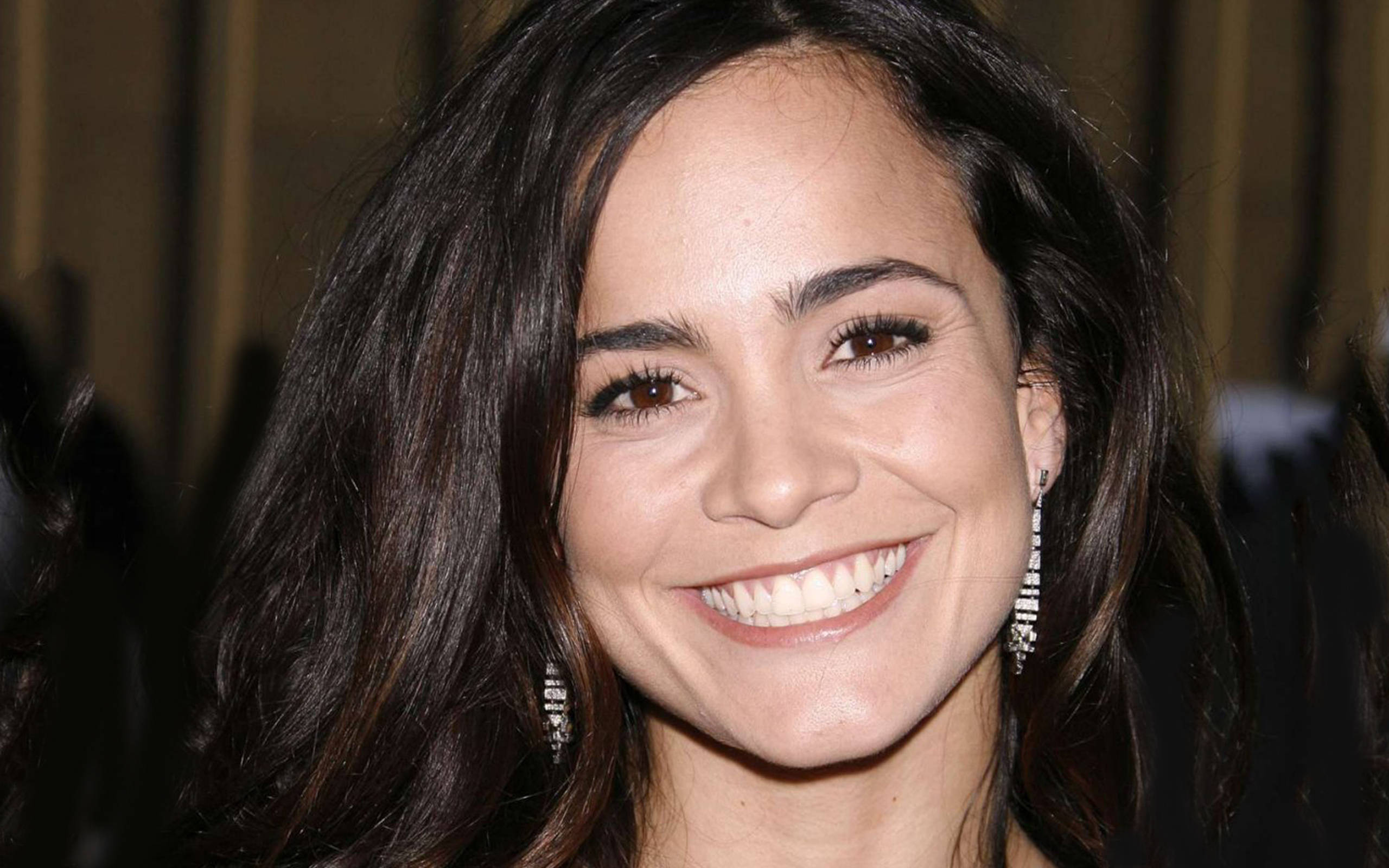 Celebrity 桌布 壁紙 — 一位光彩照人的女性，深色波浪長髮，閃爍耳環，對著鏡頭露出燦爛笑容。