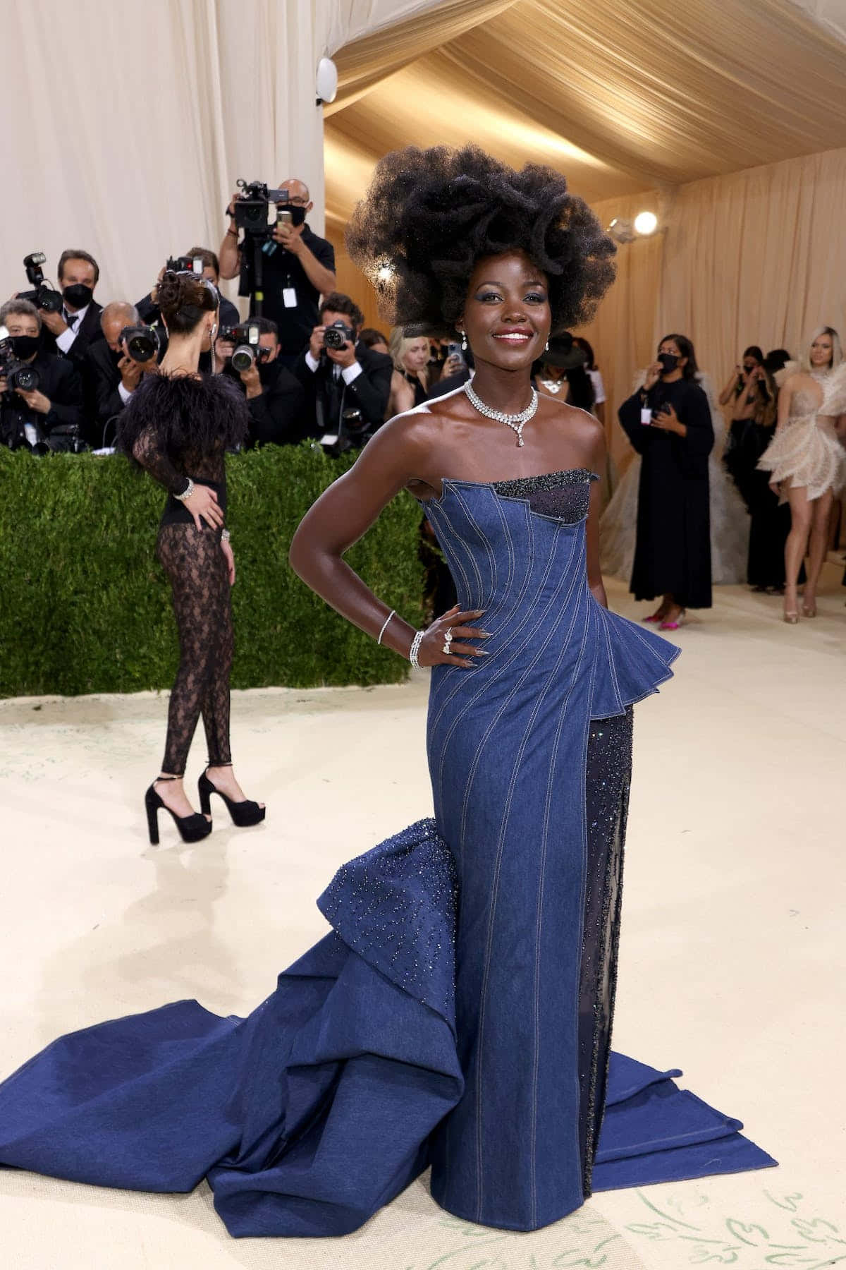 Met Gala 2021 桌布 壁紙 — 一位光彩照人的女性身穿戲劇性的藍色牛仔長裙，搭配豐滿的爆炸頭，在華麗的紅地毯活動中自信地擺姿勢。