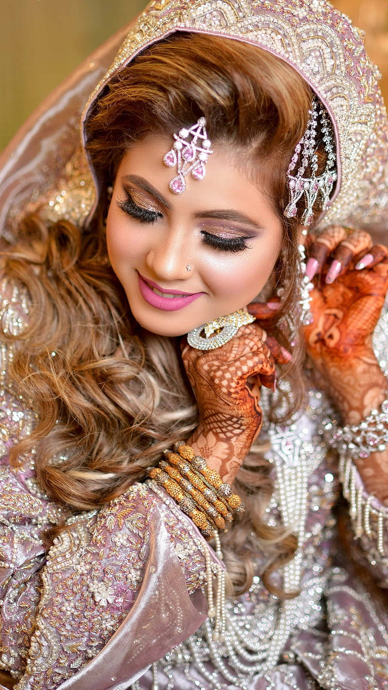Bridal 桌布 壁紙 — 一位光彩照人的新娘穿著華麗的粉紅和金色婚紗，帶著精緻的指甲花圖案和閃閃發光的珠寶，溫柔地微笑。