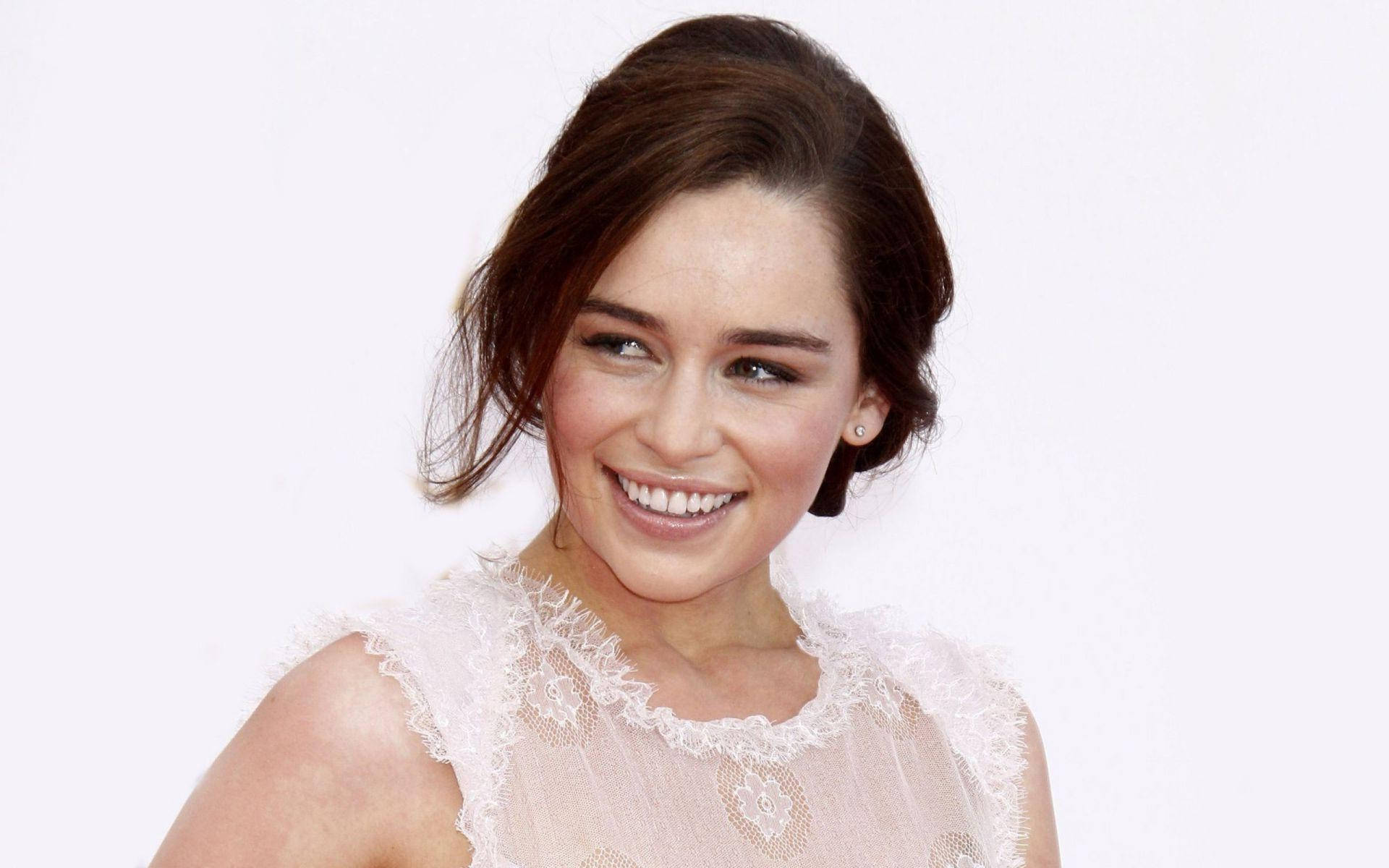 Emilia 桌布 壁紙 — 一位光彩照人的棕髮女性，穿著精緻的白色蕾絲上衣，在純白背景前溫暖微笑。