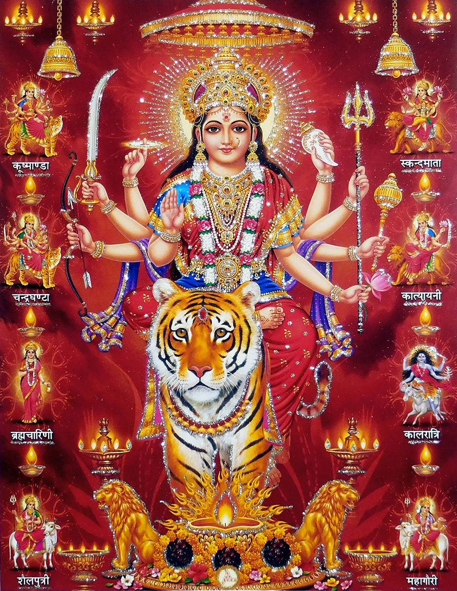 Durga 桌布 壁紙 — 一位光芒四射、多臂的印度教女神杜爾迦，身披金紅裝飾，坐在一頭兇猛的老虎上，周圍有神聖符號和較小的女神，背景是發光的紅色。
