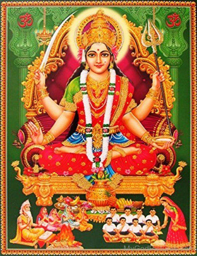Goddess 桌布 壁紙 — 一位光芒四射的四臂印度教女神坐在金色寶座上，身穿紅綠服飾，手持武器和碗，周圍有信徒。