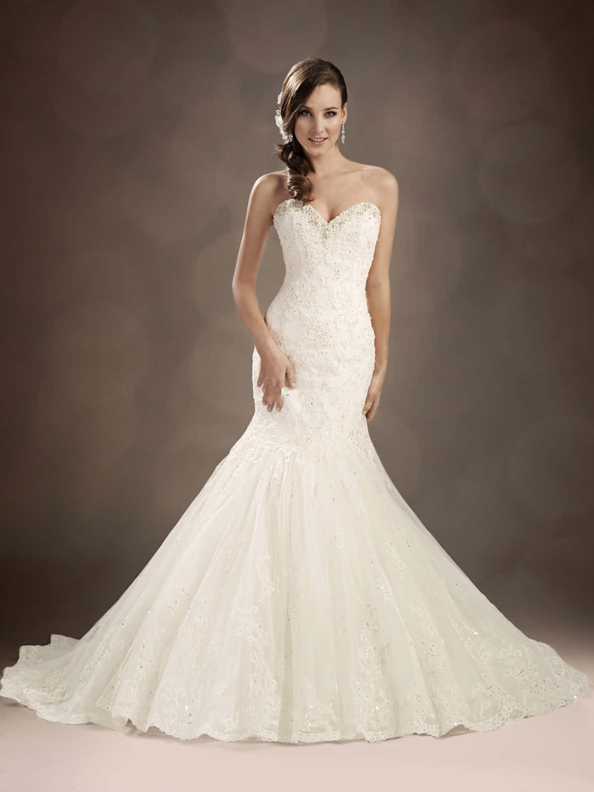 Wedding Gown 桌布 壁紙 — 一位光芒四射的新娘身穿優雅的白色美人魚婚紗，帶有精緻的蕾絲細節和飄逸的裙擺，在柔和的棕色背景前優雅地擺姿勢。