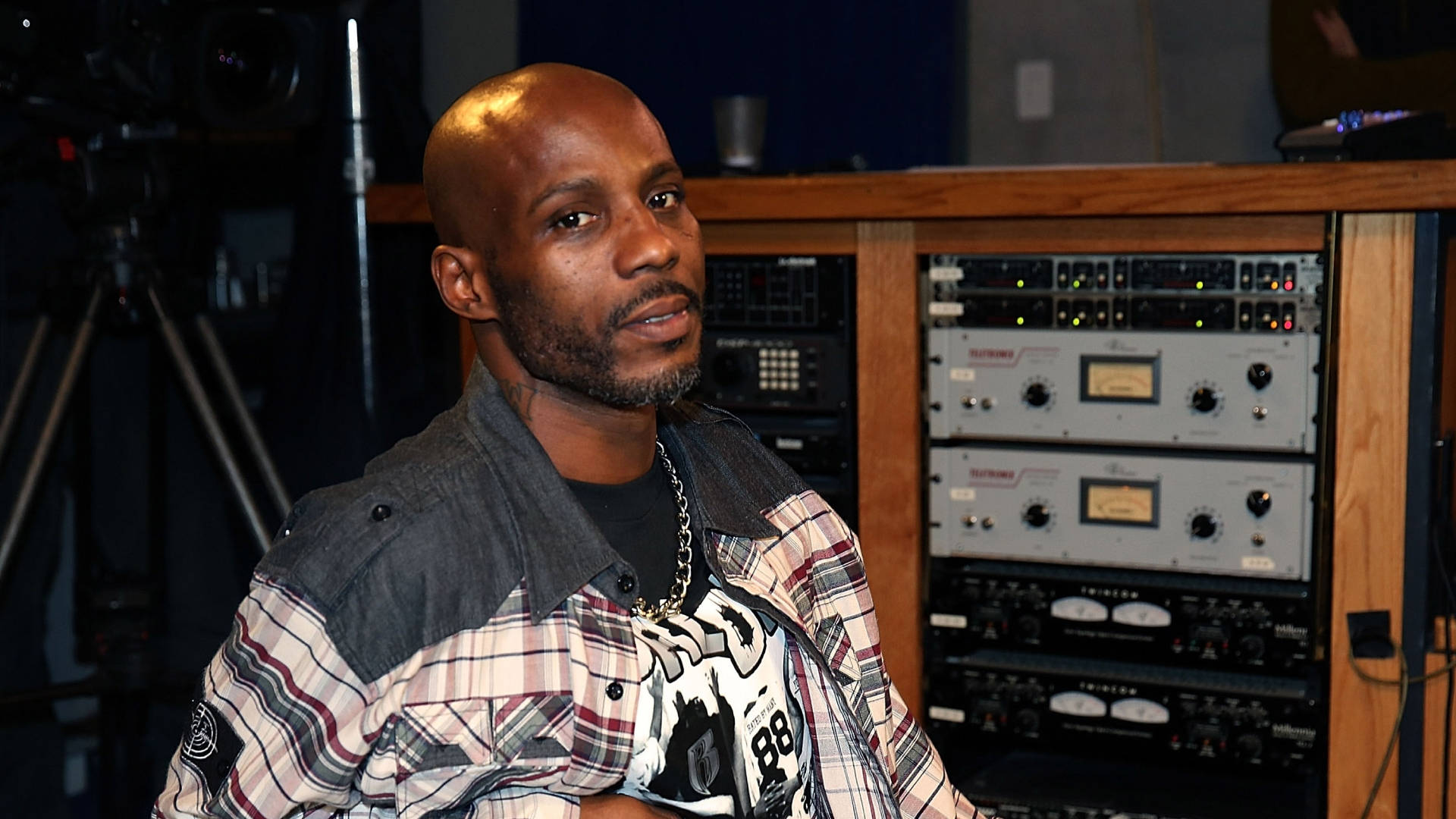 Dmx 桌布 壁紙 — 一位光頭、留鬍子的黑人男性，身穿格紋襯衫和戴著鏈條，坐在一個背後有音響設備的錄音室裡。