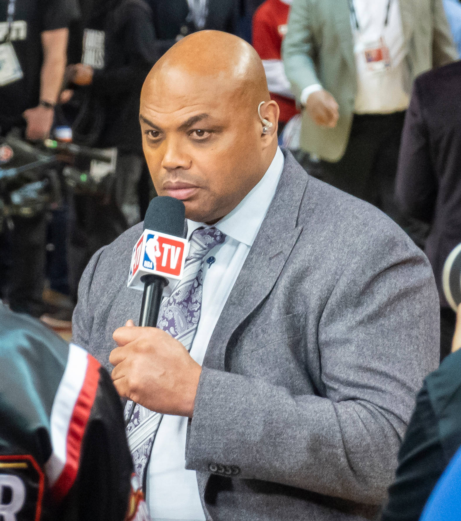 NBA 桌布 壁紙 — 一位光頭NBA TV體育記者穿著灰色西裝，手持麥克風，專注地看著鏡頭。
