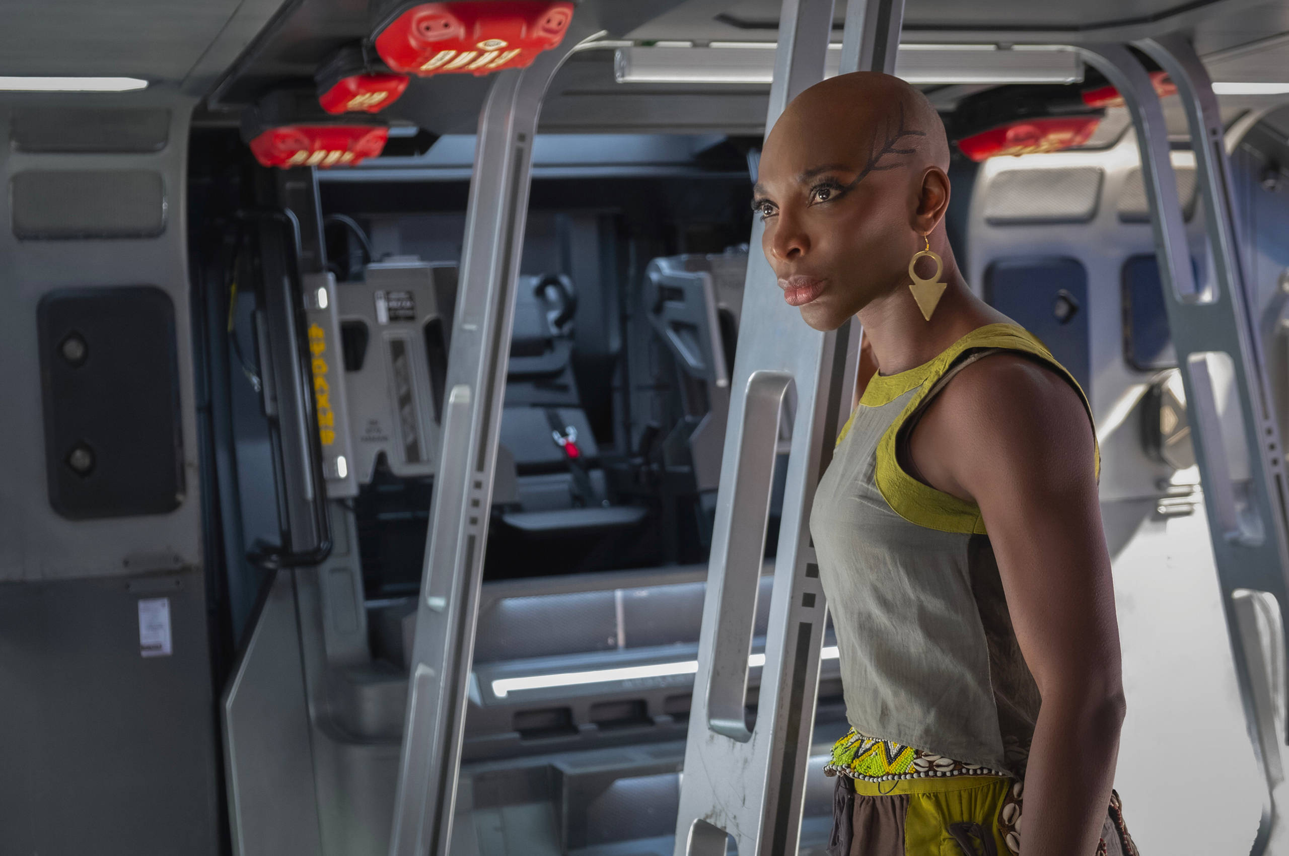 Wakanda 桌布 壁紙 — 一位光頭女性臉上帶有幾何圖案標記，站在由紅色頭頂燈光照亮的未來主義太空船走廊中。