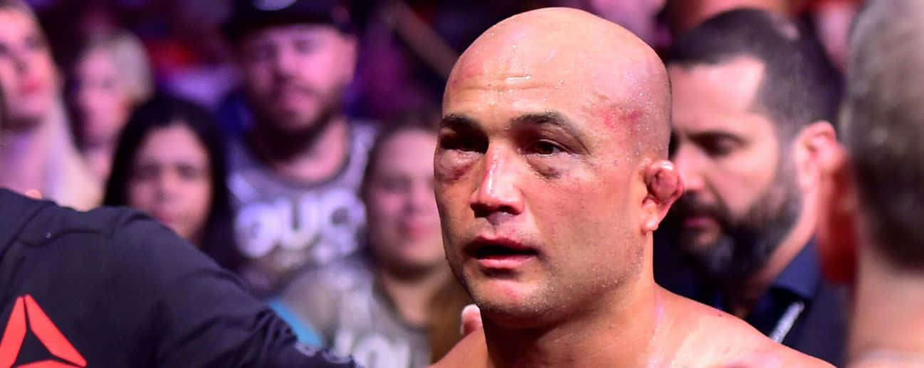 UFC 桌布 壁紙 — 一位光頭戰士帶著瘀傷的眼睛，在明亮的燈光下於擁擠的競技場中凝視著。