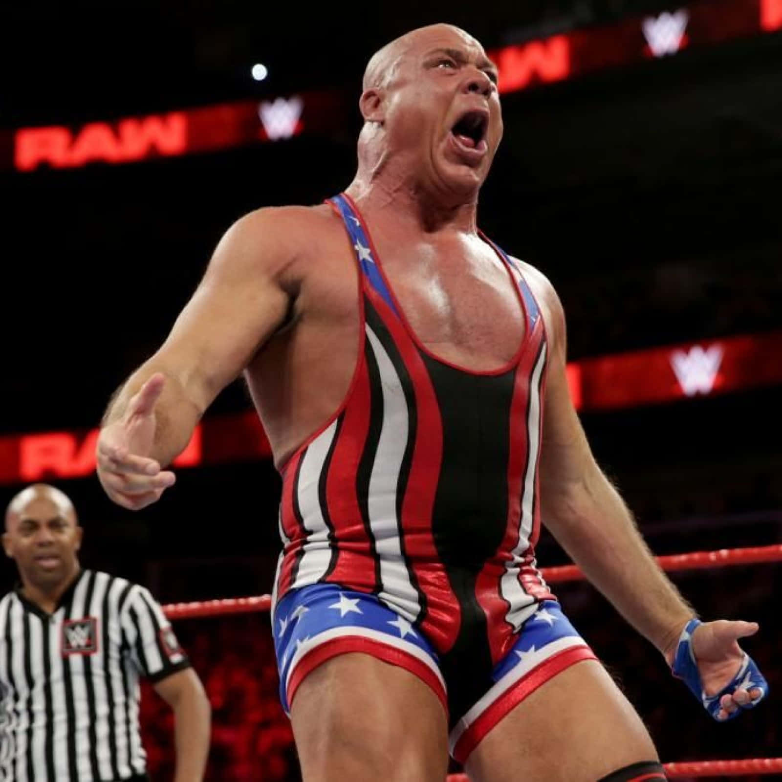 WWE 桌布 壁紙 — 一位光頭摔角手穿著紅白藍愛國緊身衣，在摔角場上勝利咆哮，背景有裁判。
