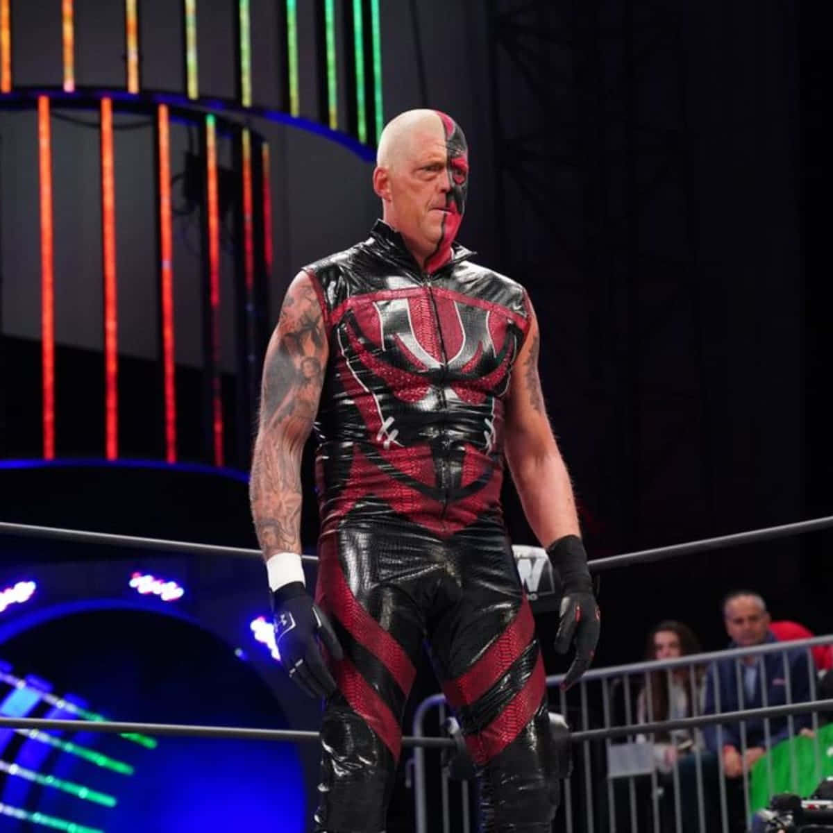 WWE 桌布 壁紙 — 一位光頭摔角手穿著紅黑服裝，站在一個背後有發光垂直燈光的擂台上。