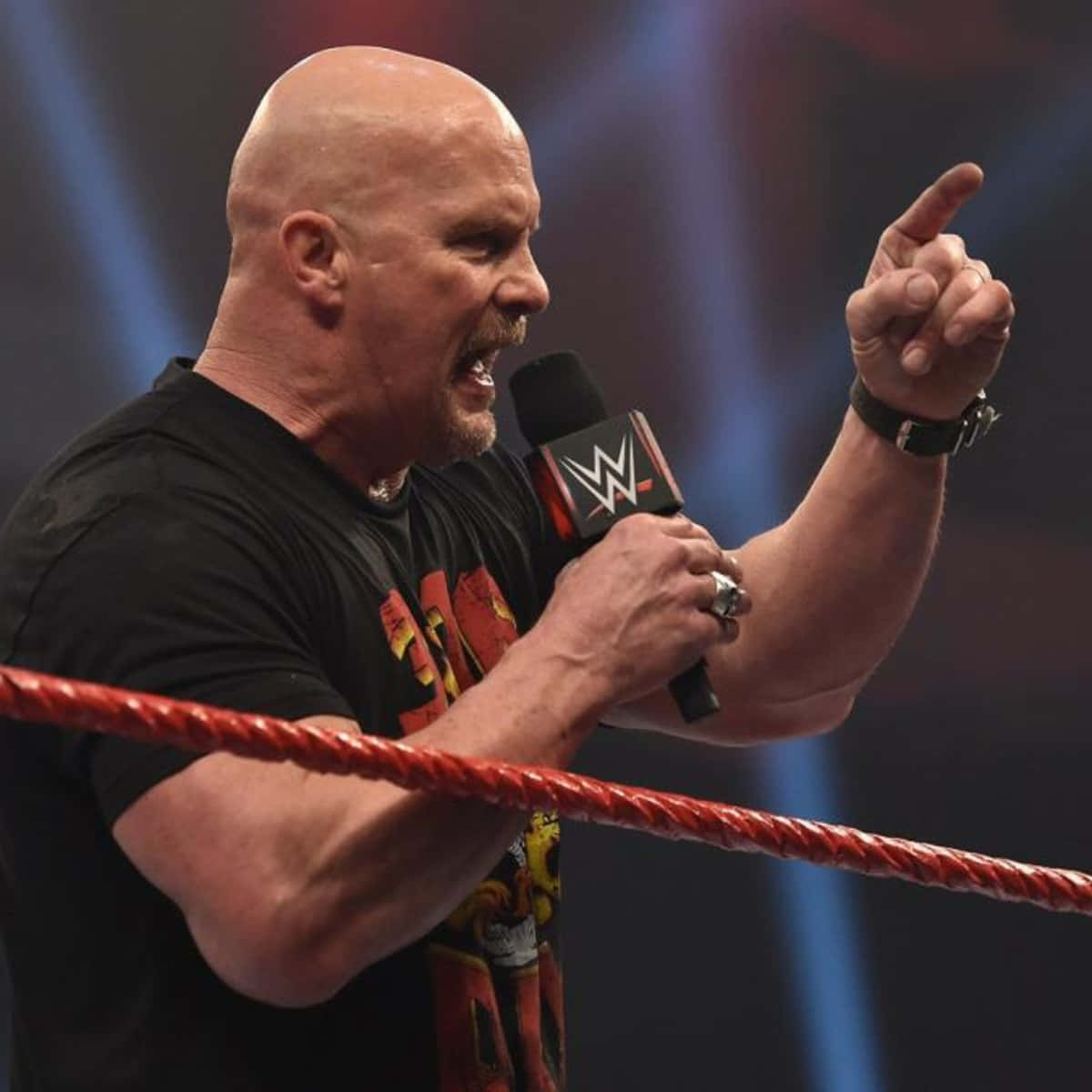 WWE 桌布 壁紙 — 一位光頭摔角手穿著黑色襯衫，在摔角場內一邊激動地指著一邊對著WWE麥克風大叫。