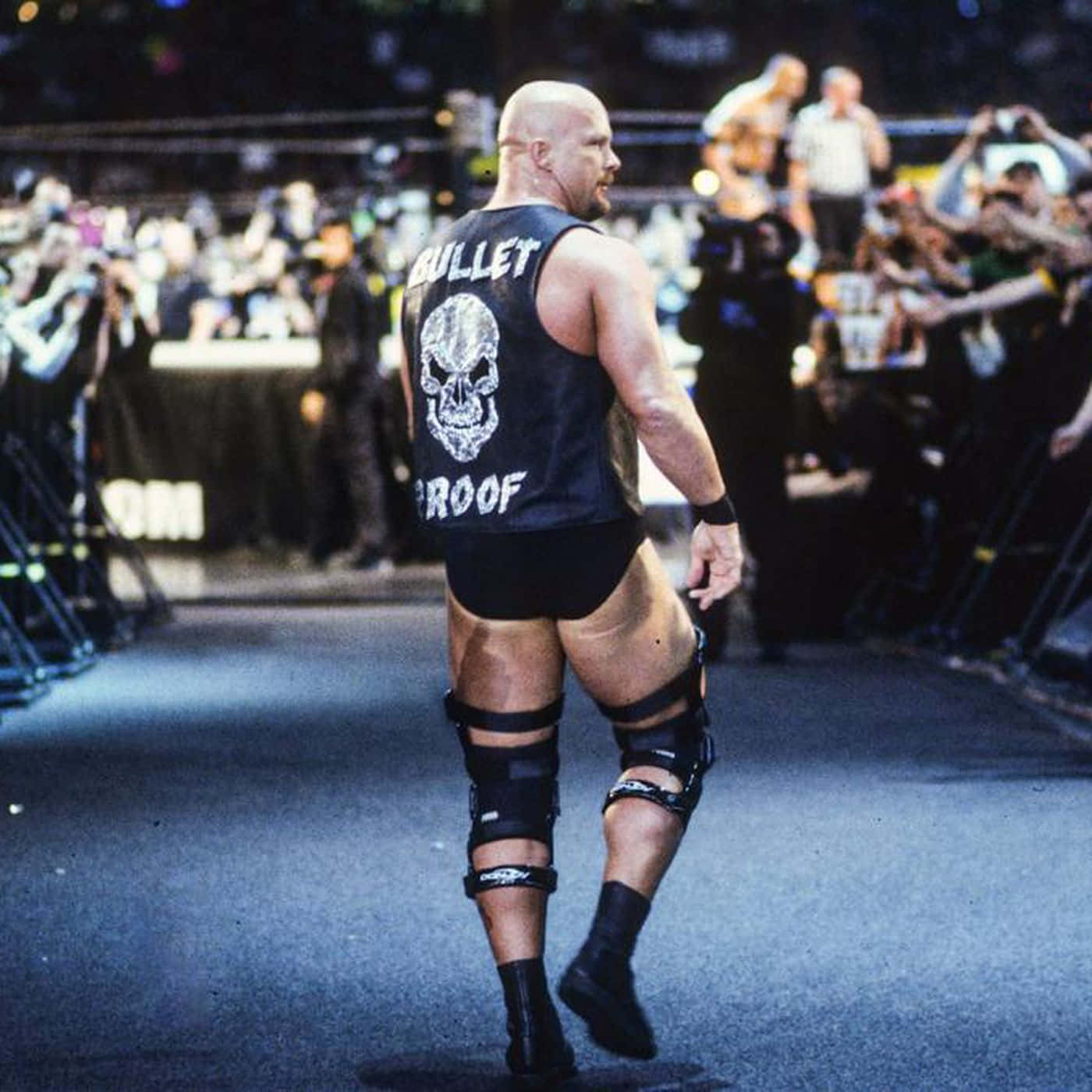 WWE 桌布 壁紙 — 一位光頭摔角手身穿印有骷髏標誌的黑色背心，自信地沿著斜坡走向摔角賽事中歡呼的人群。