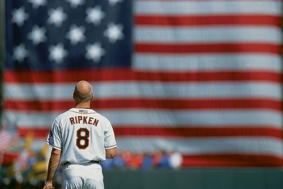 cal ripken jr 桌布 壁紙 — 一位光頭棒球運動員穿著Ripken 8球衣，背對鏡頭，面向一面大型模糊的美國國旗。