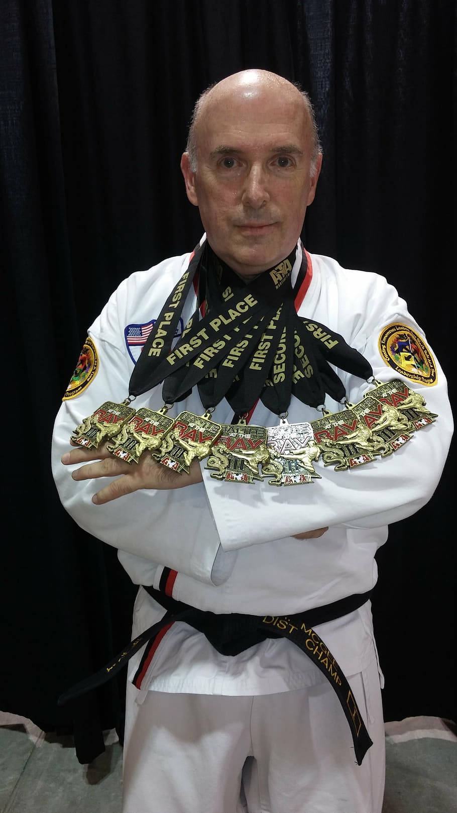 martial arts 桌布 壁紙 — 一位光頭武術家身穿白色道服，腰繫黑帶，自豪地展示掛在頸上的眾多第一名獎牌。