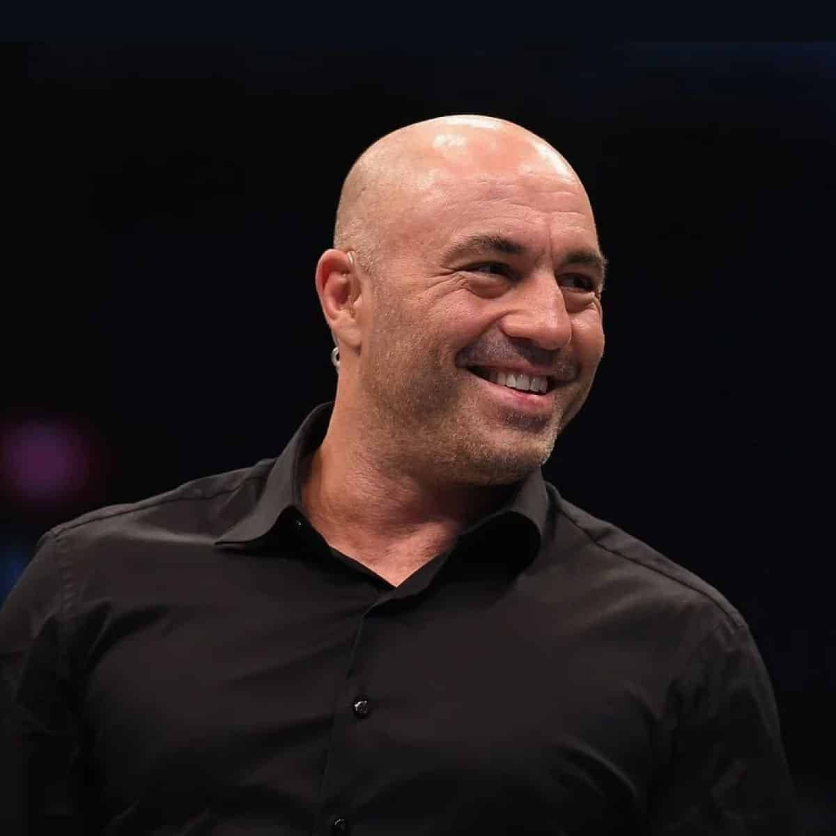 Smile 桌布 壁紙 — 一位光頭男士帶著溫暖的笑容和鬍渣，身穿黑色襯衫，背景是帶有柔和散景燈光的暗色調。