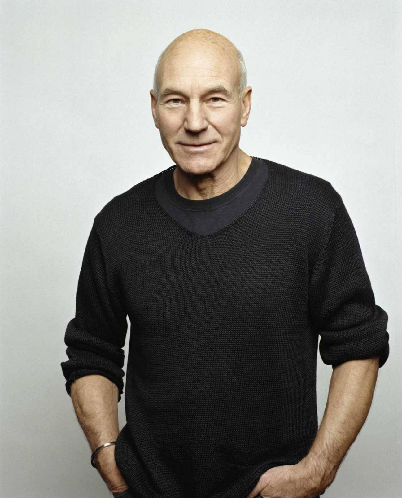 Celebrity 桌布 壁紙 — 一位光頭男士穿著黑色紋理毛衣，在純淺灰色工作室背景前溫柔微笑。