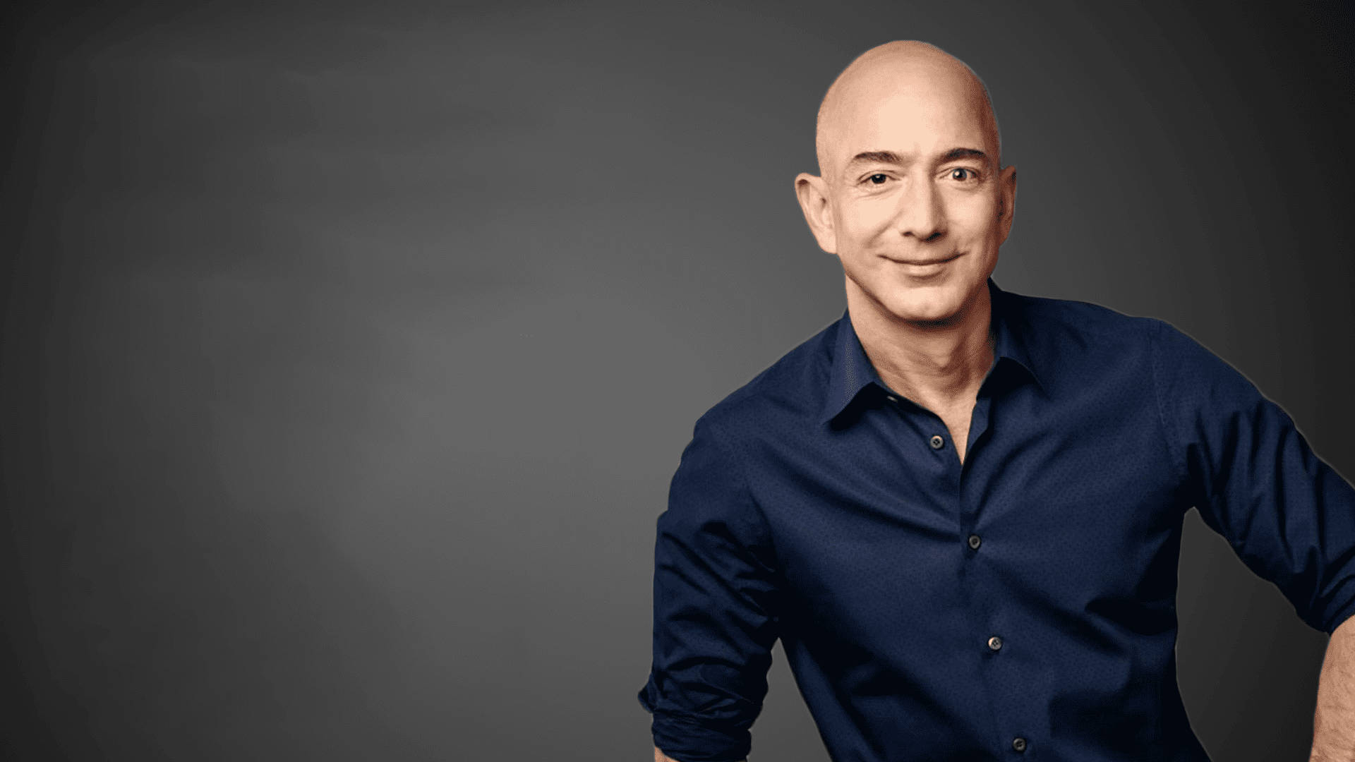 Bezos 桌布 壁紙 — 一位光頭男士身穿深藍色襯衫，在深灰色工作室背景前自信微笑。