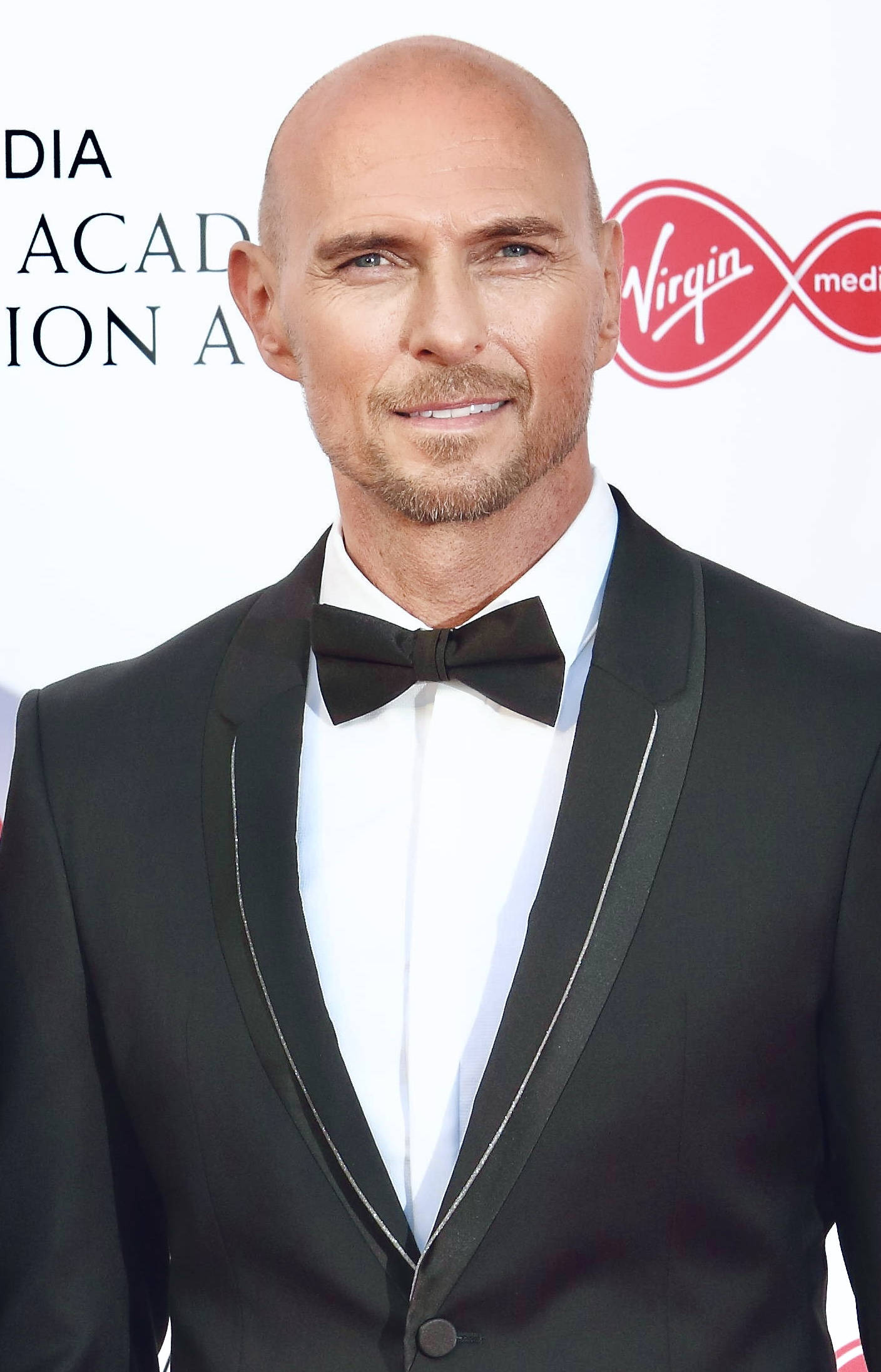 Celebrity 桌布 壁紙 — 一位光頭留山羊鬍的男人，身穿黑色銀邊禮服和領結，在媒體頒獎活動中微笑。