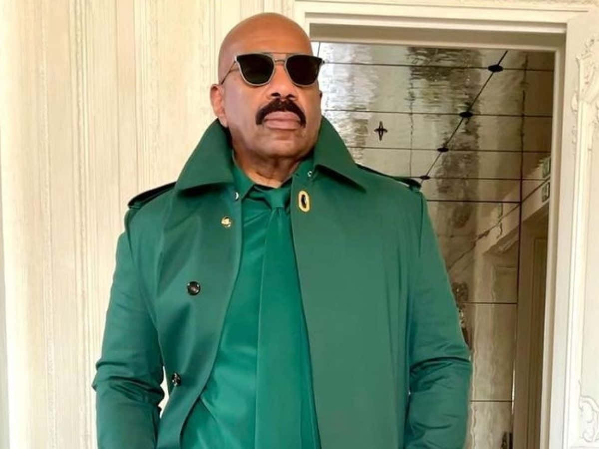 steve harvey 桌布 壁紙 — 一位光頭留鬍鬚的男人，穿著大膽的綠色風衣和太陽眼鏡，站在華麗的門口。