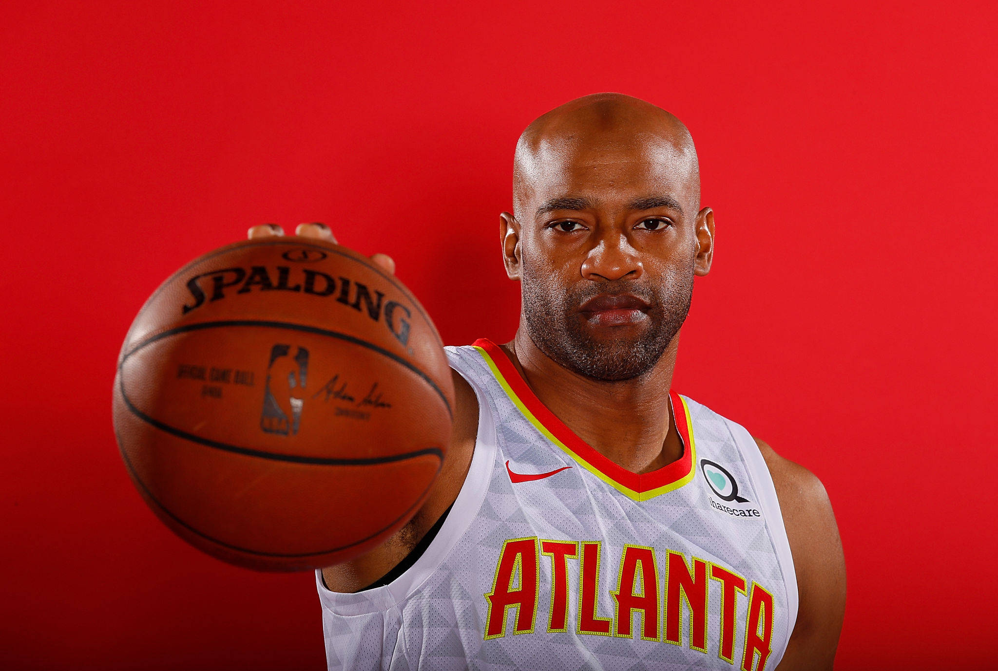 NBA 桌布 壁紙 — 一位光頭籃球運動員穿著亞特蘭大球衣，在純紅色背景前拿著一個Spalding籃球。