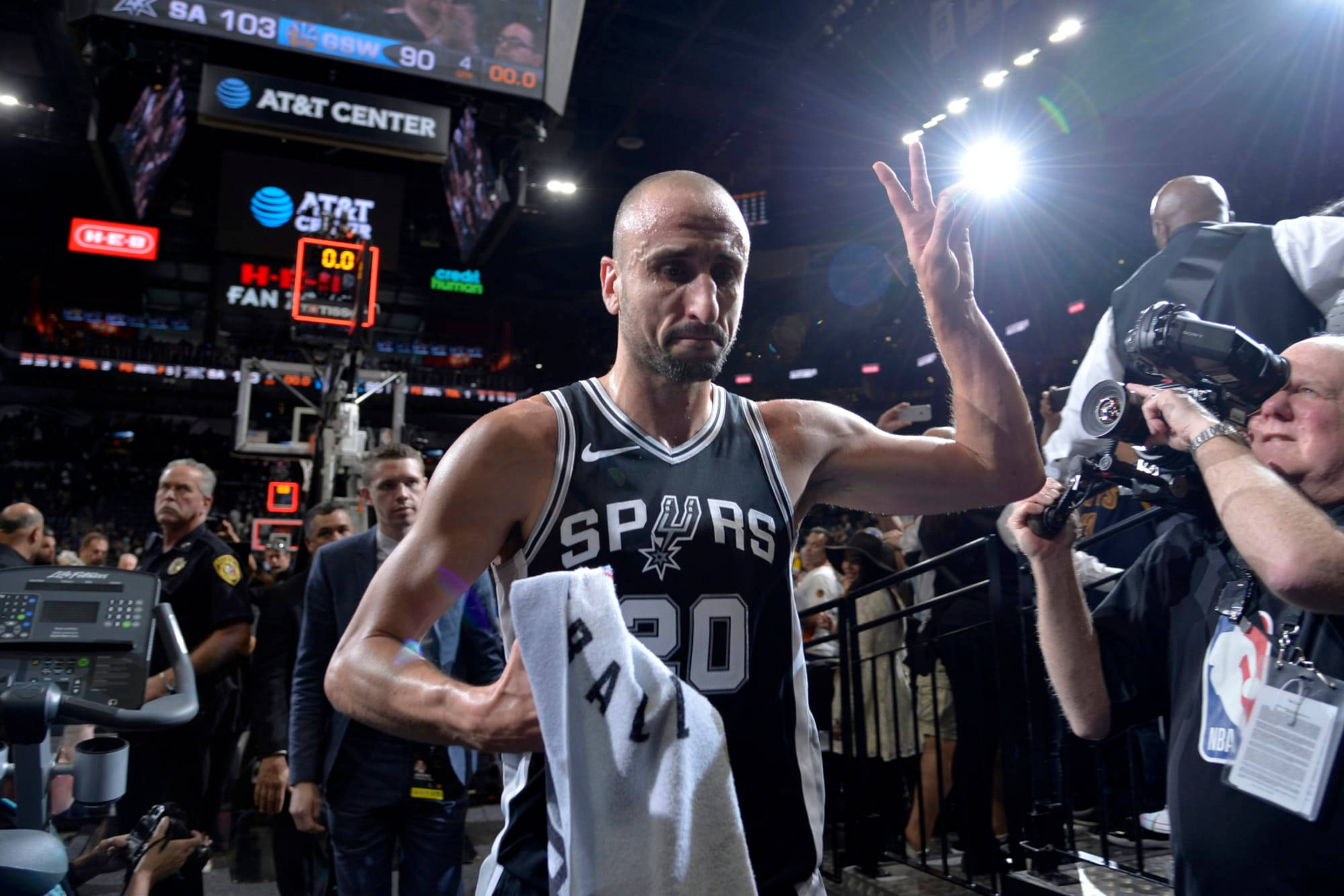 Manu 桌布 壁紙 — 一位光頭籃球運動員穿著馬刺隊球衣，在明亮的場館燈光下比賽結束後離場時向球迷揮手。