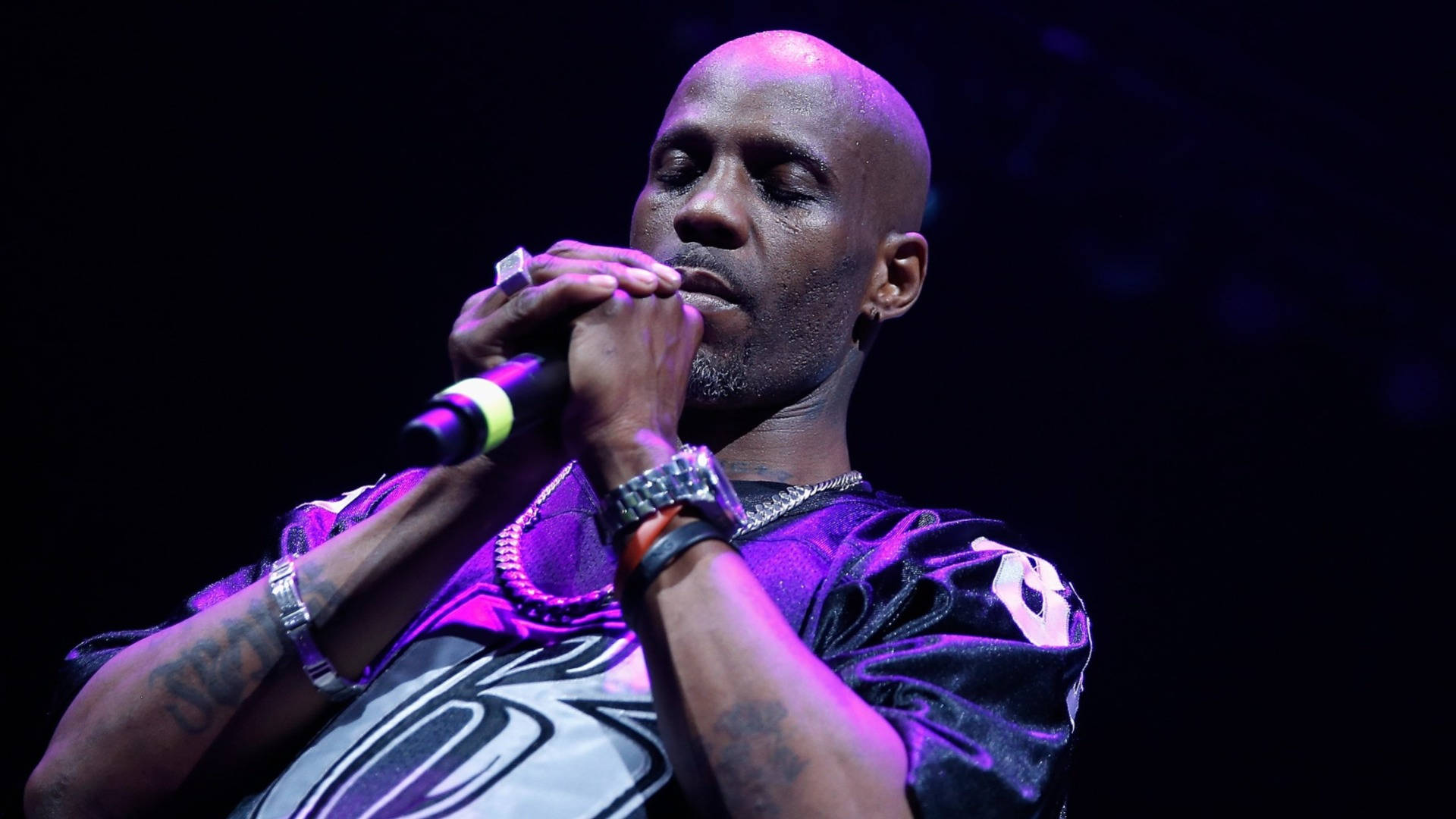 DMX 桌布 壁紙 — 一位光頭紋身男表演者在紫色舞台燈光下對著麥克風唱歌，背景為深色。