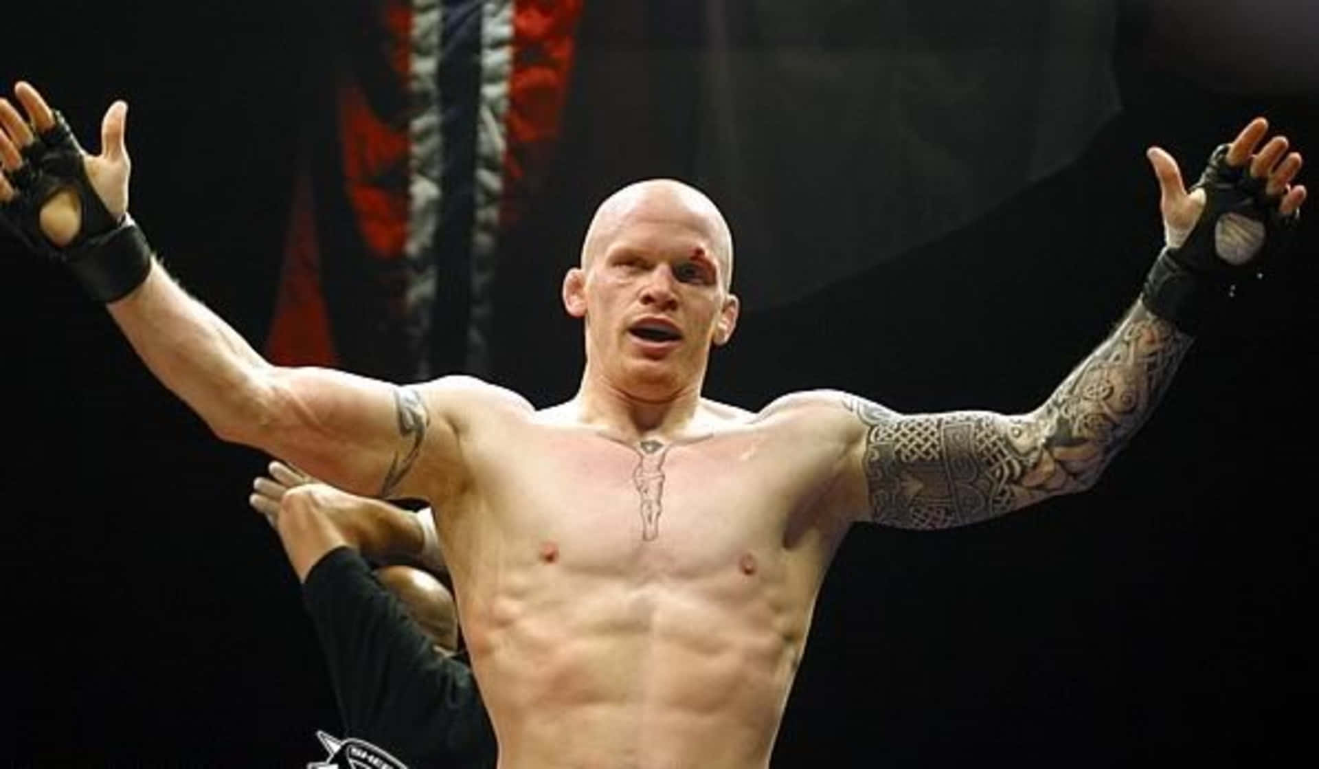 MMA 桌布 壁紙 — 一位光頭肌肉發達的戰士，身上有刺青，在昏暗的競技場中高舉雙臂慶祝勝利。