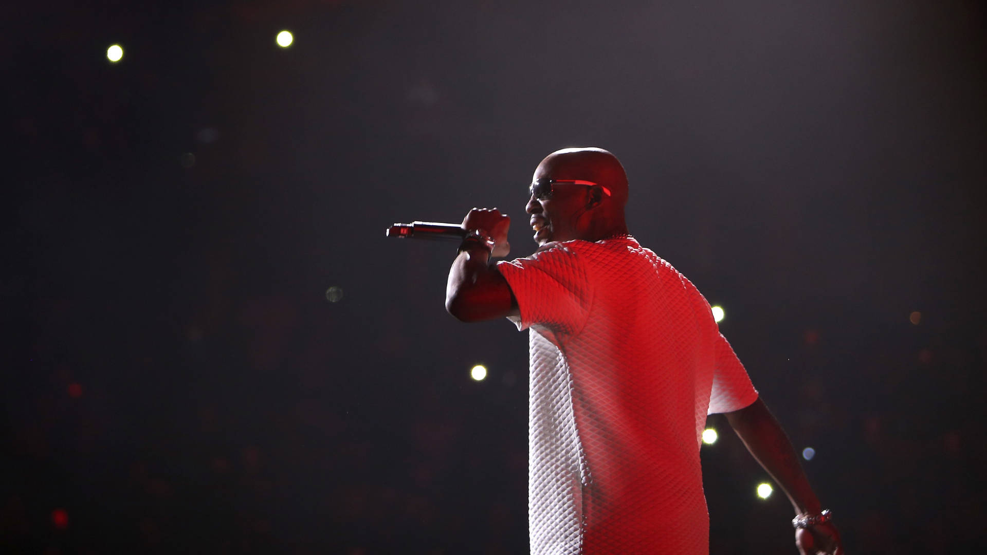 DMX 桌布 壁紙 — 一位光頭表演者穿著紅色質感襯衫，在黑暗背景的舞台燈光下對著麥克風唱歌。