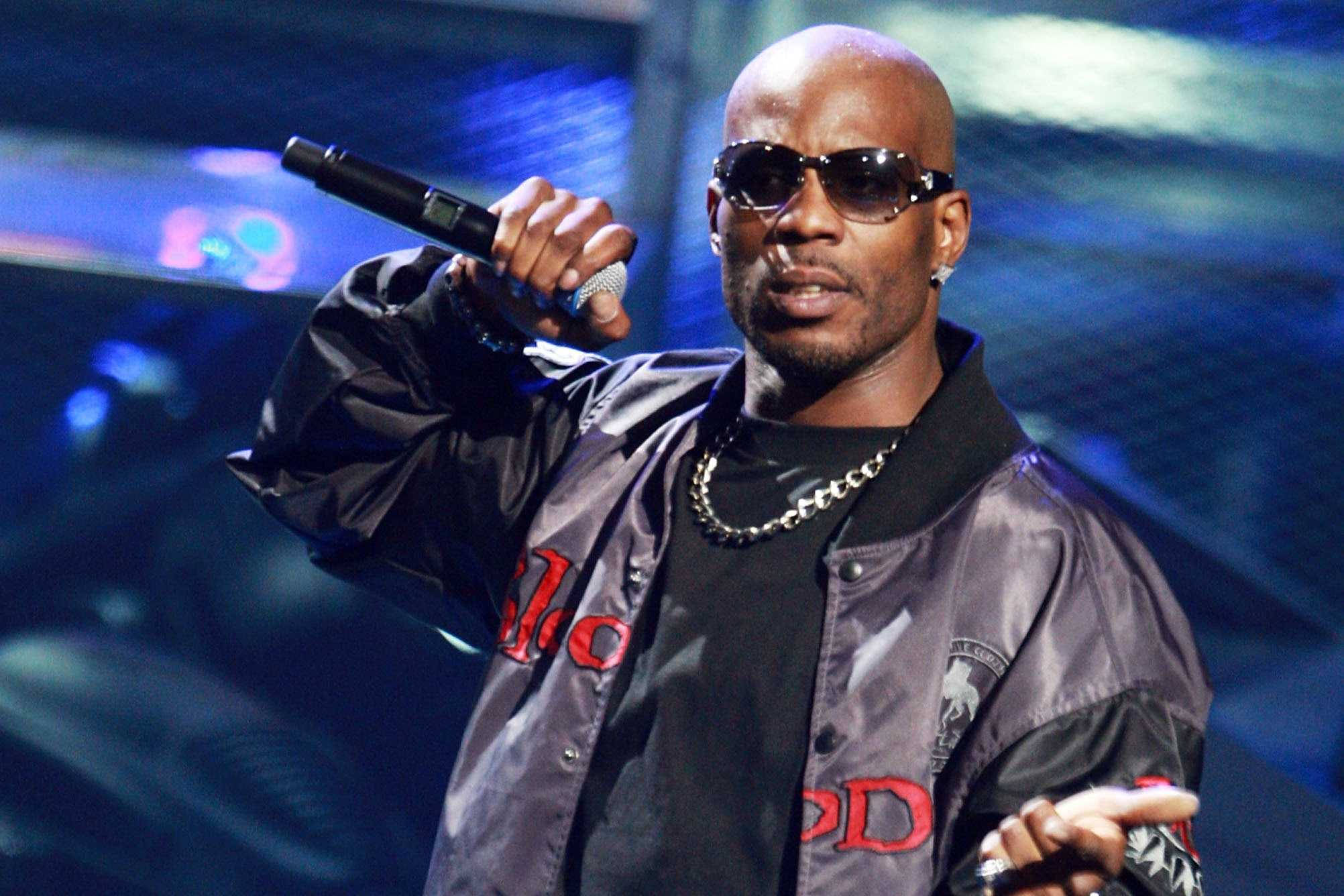 DMX 桌布 壁紙 — 一位光頭說唱歌手戴著太陽眼鏡和飛行員夾克，在藍色舞台燈光下拿著麥克風。