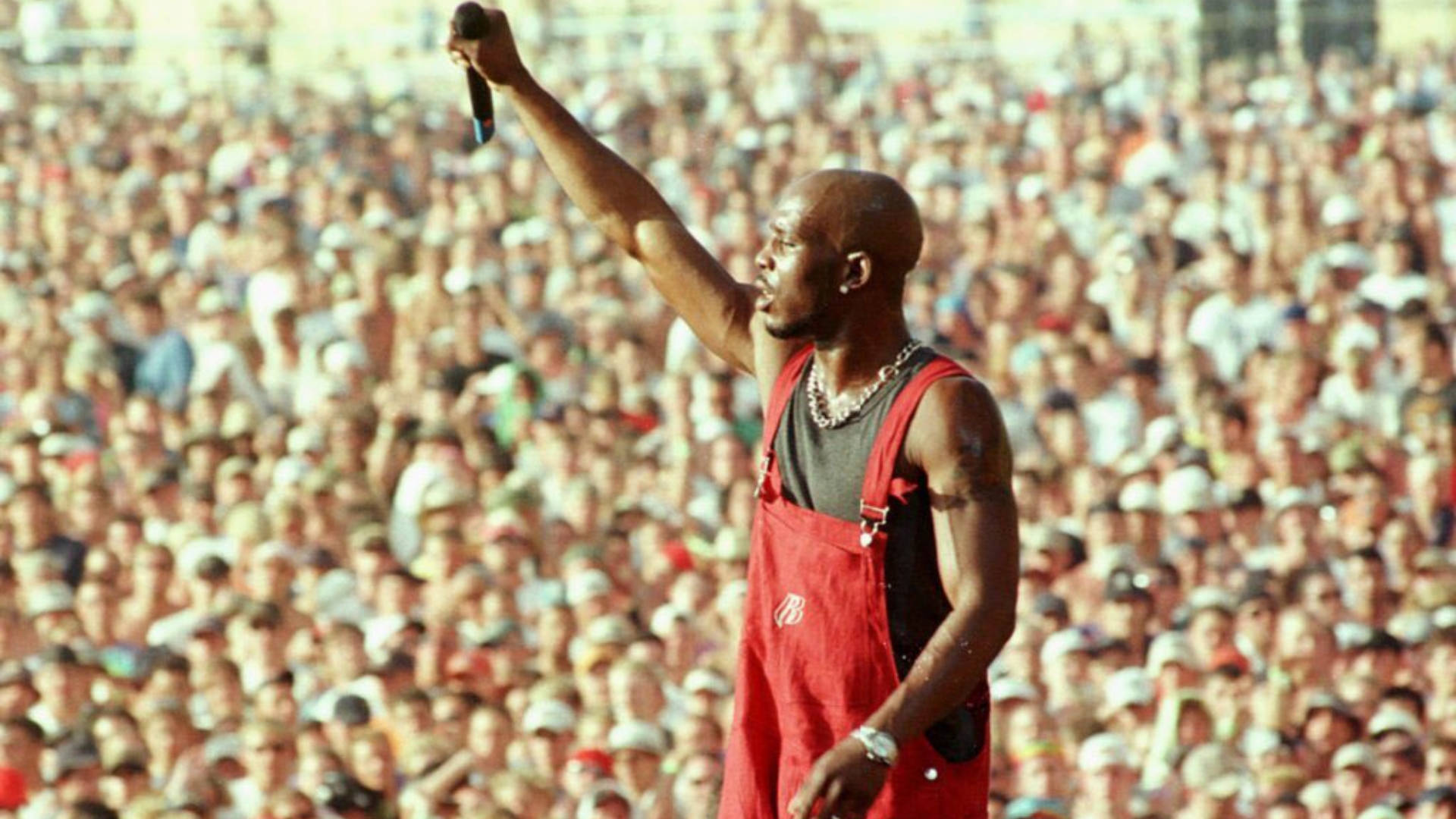 DMX 桌布 壁紙 — 一位光頭饒舌歌手穿著紅色連身褲，向陽光普照的體育場人群舉起麥克風。