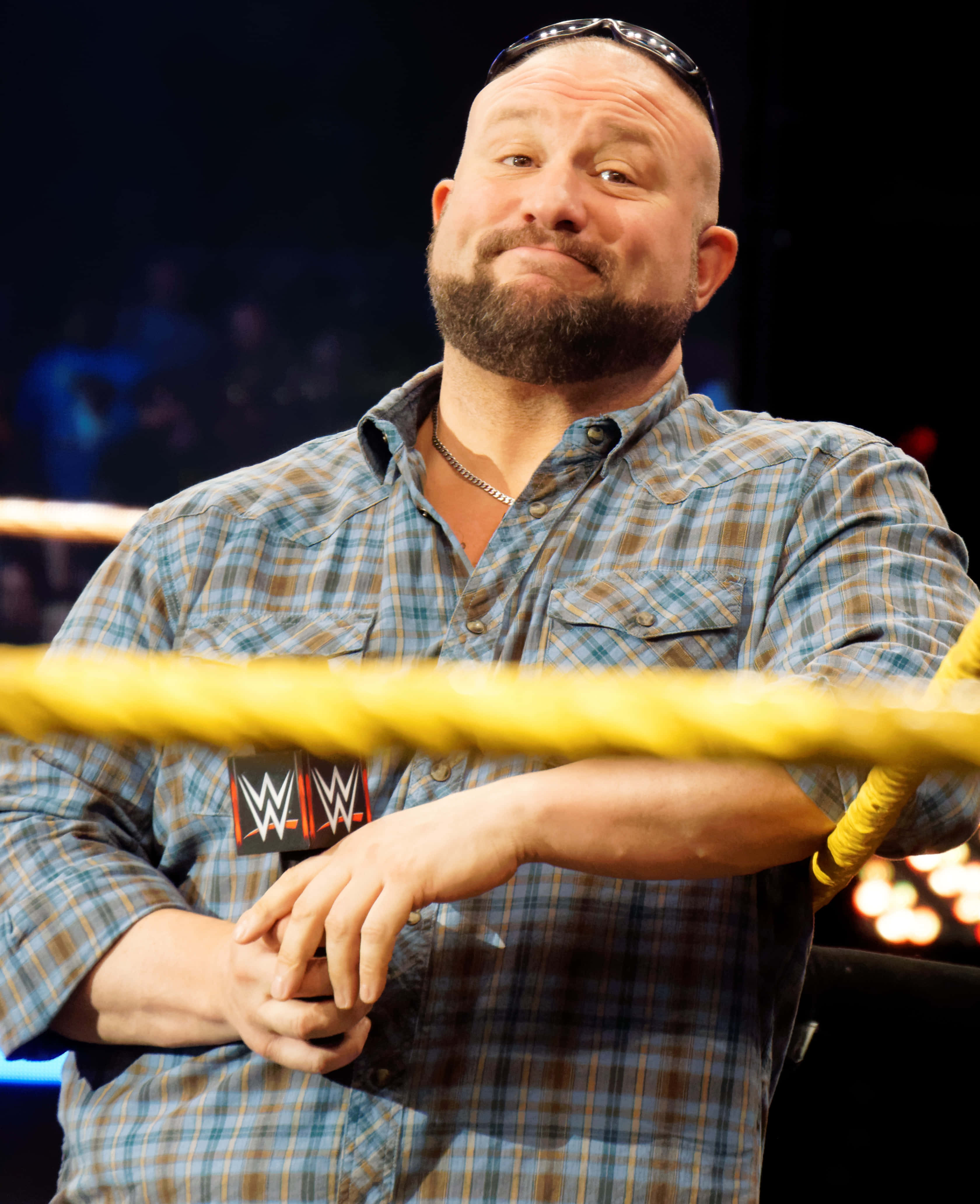 Wrestling 桌布 壁紙 — 一位光頭鬍鬚摔角手身穿格紋襯衫，自信地微笑靠在摔角擂台繩索上。