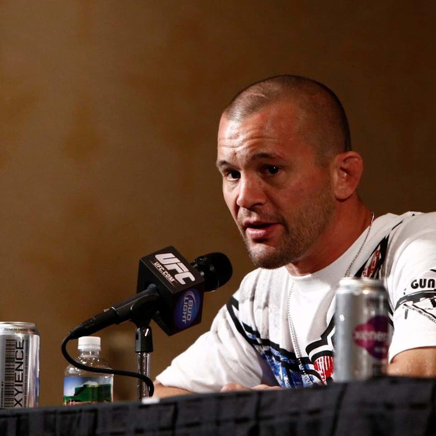 UFC 桌布 壁紙 — 一位光頭鬍鬚男在記者會桌上對著UFC麥克風說話，桌上有飲料。