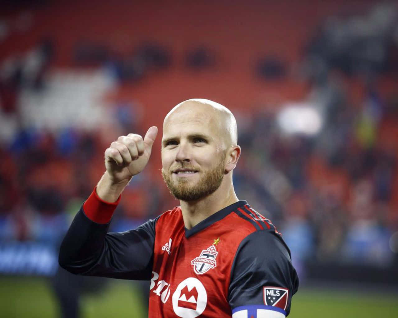 Athlete 桌布 壁紙 — 一位光頭鬍鬚的足球員，身穿紅黑多倫多FC球衣，在球場向球迷豎起大拇指。