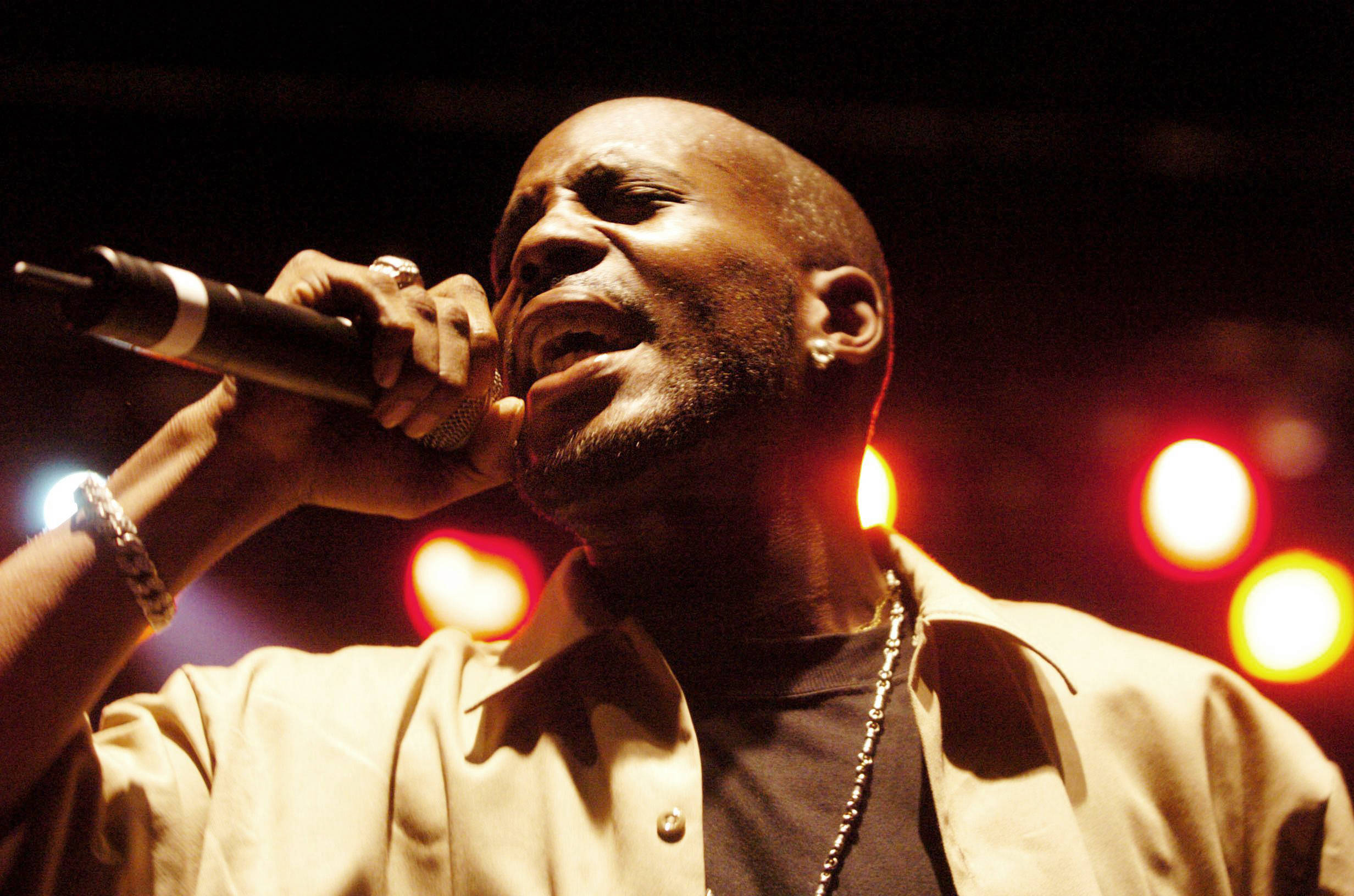 Dmx 桌布 壁紙 — 一位光頭黑人男子在溫暖的舞台燈光下熱情地對著麥克風唱歌，背景有模糊的紅色和黃色散景。