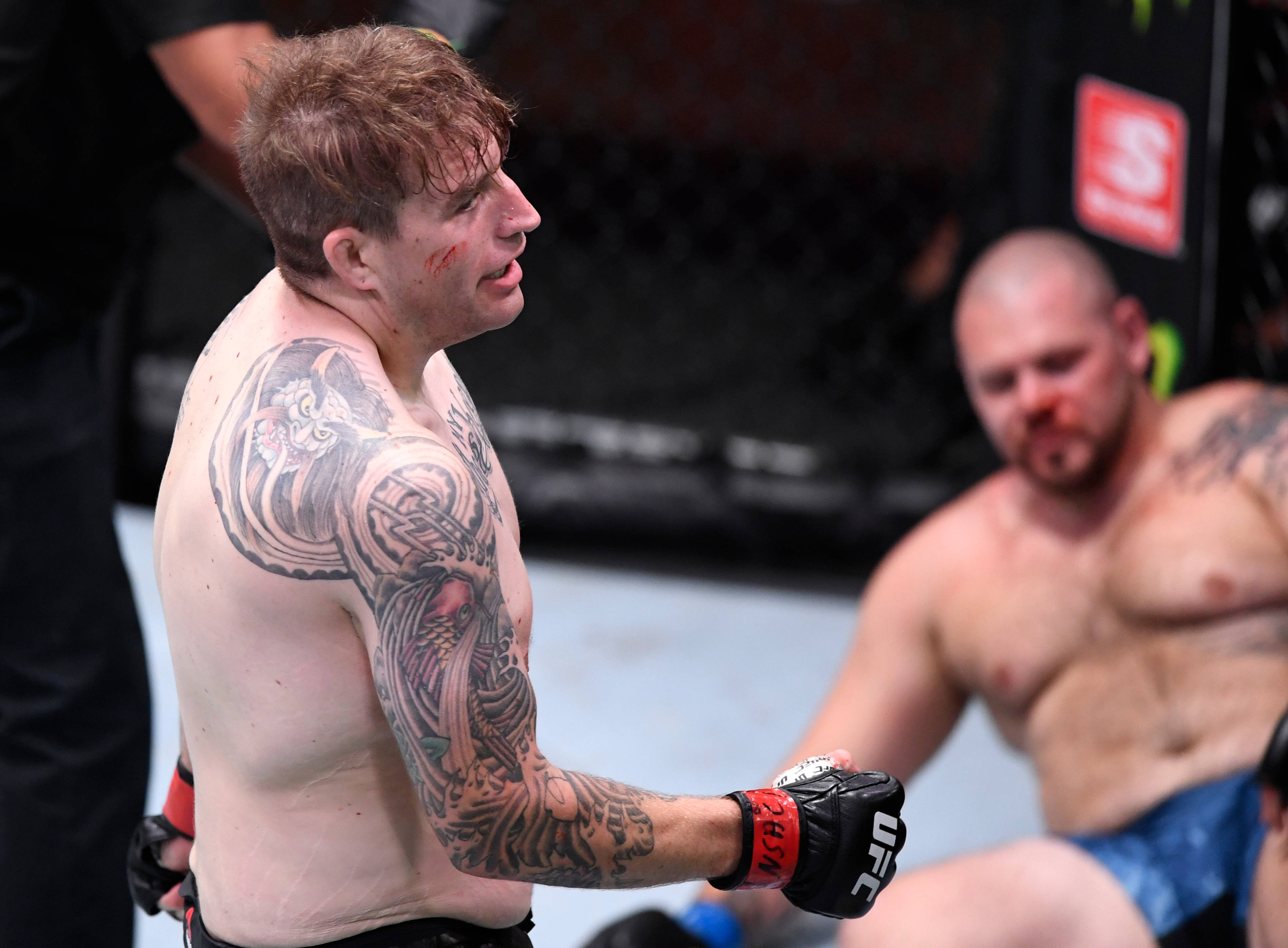 UFC 桌布 壁紙 — 一位刺青MMA拳手滿臉鮮血，在八角籠中勝利站立，而對手則坐地敗北。