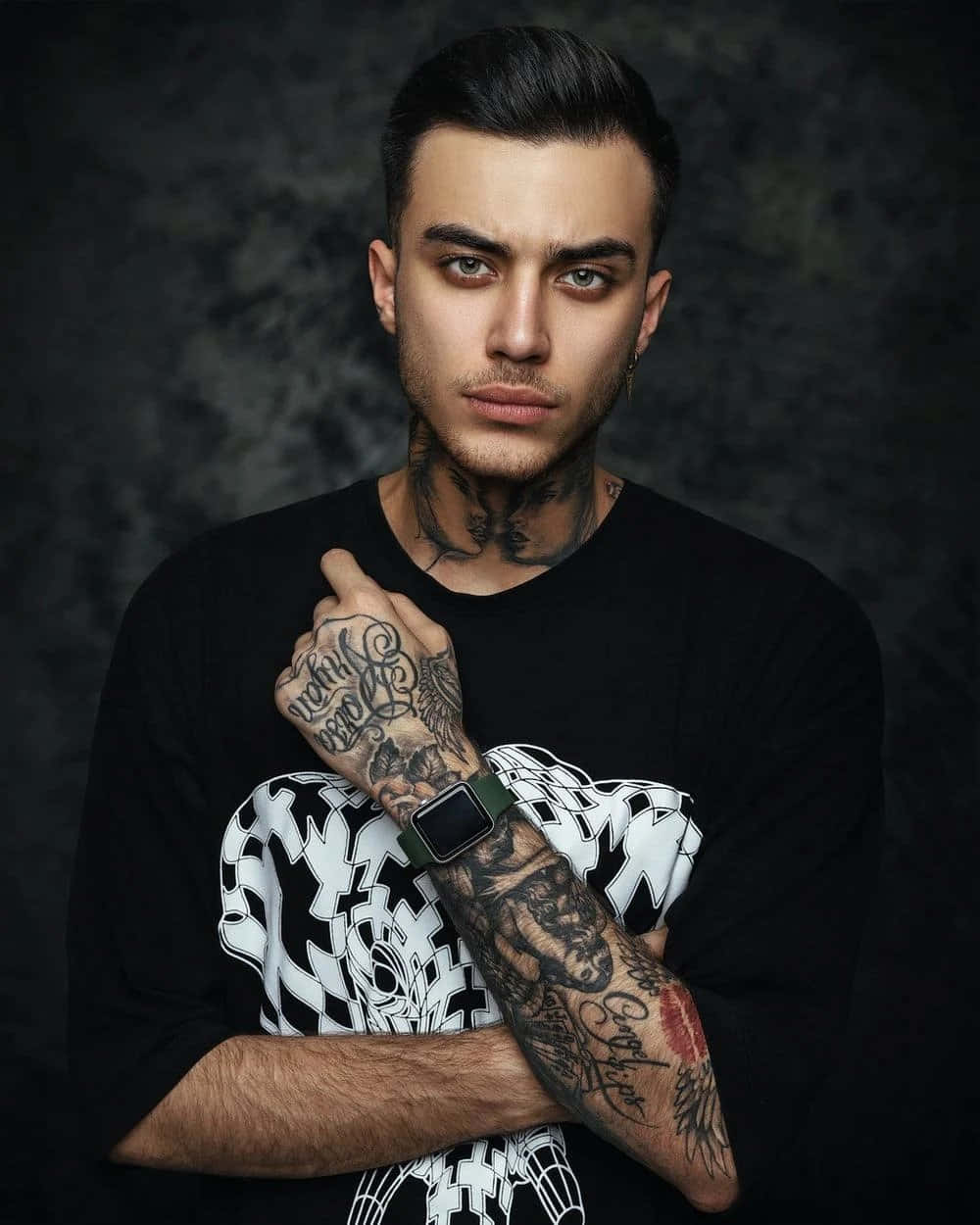Tattoo Boy 桌布 壁紙 — 一位刺青男子，眼神銳利，雙臂交叉，在深色紋理工作室背景前擺姿勢。