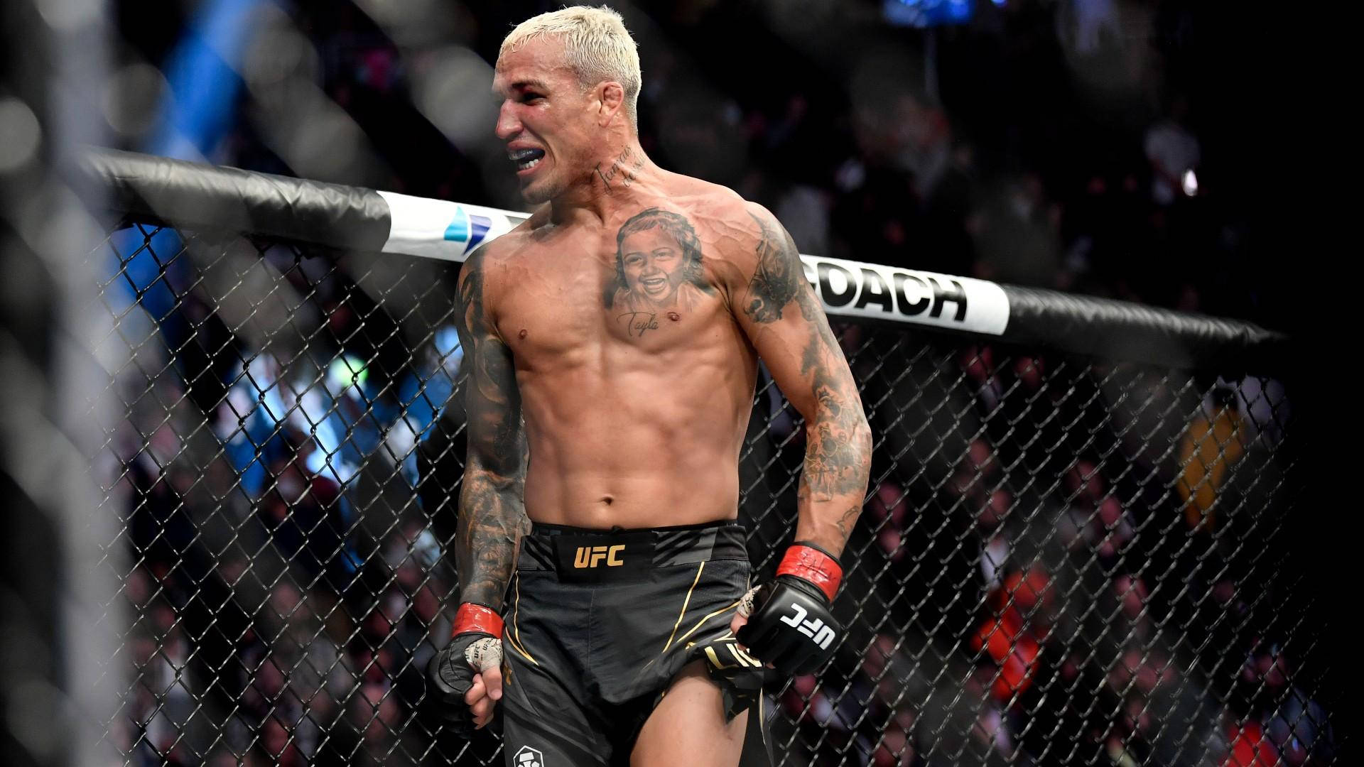 MMA 桌布 壁紙 — 一位刺青的MMA拳手穿著黑色UFC短褲，站在八角籠內，圍欄後面有群眾。