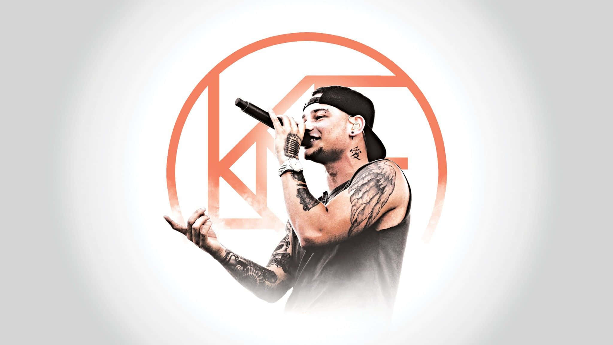 Kane Brown 桌布 壁紙 — 一位刺青說唱歌手戴著黑色帽子穿著背心，在發光的橙色圓形標誌背景下熱情地對著麥克風說唱。