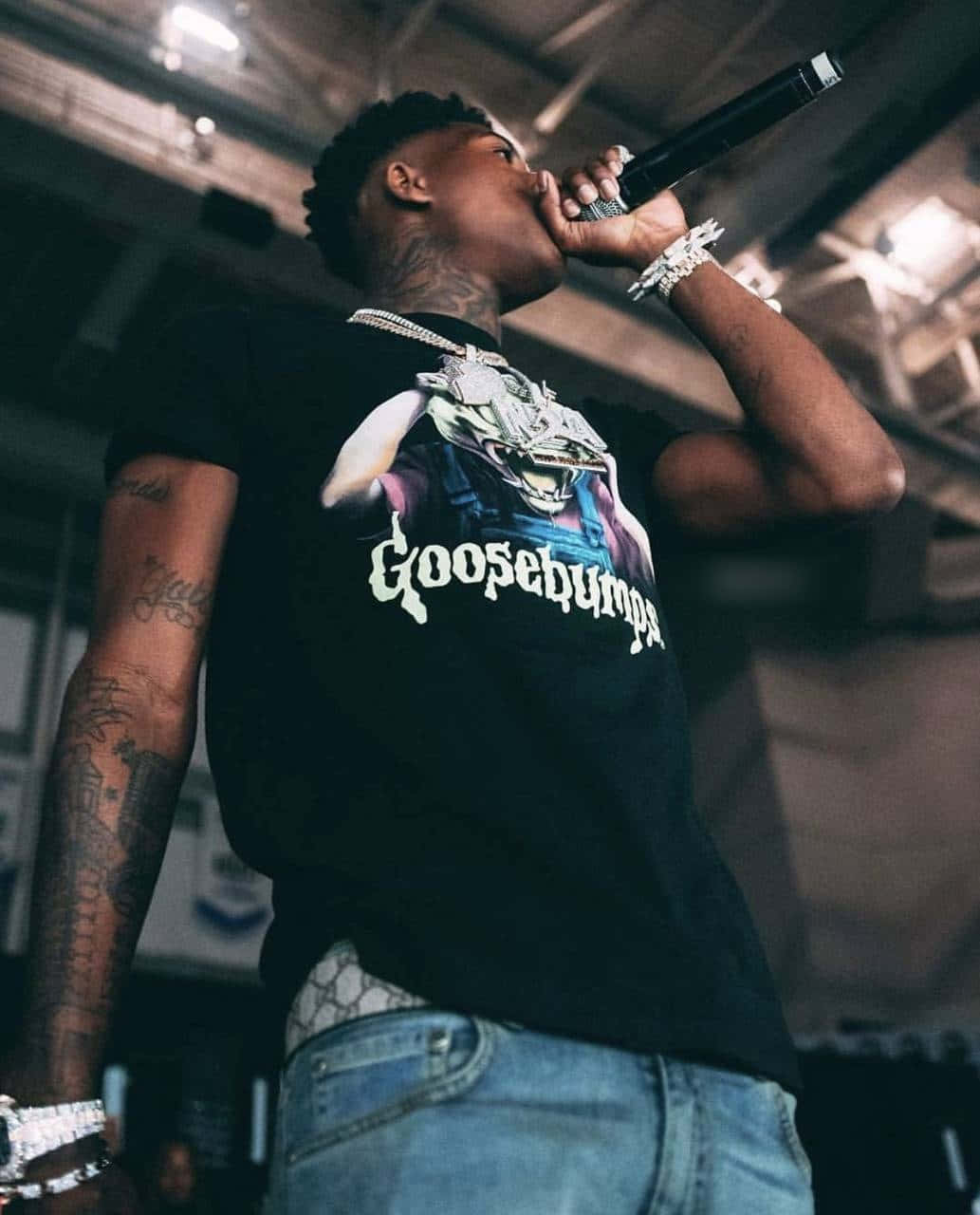 NBA YoungBoy 桌布 壁紙 — 一位刺青說唱歌手穿著 Goosebumps T恤，在昏暗的演唱會燈光下熱情地對著麥克風表演。