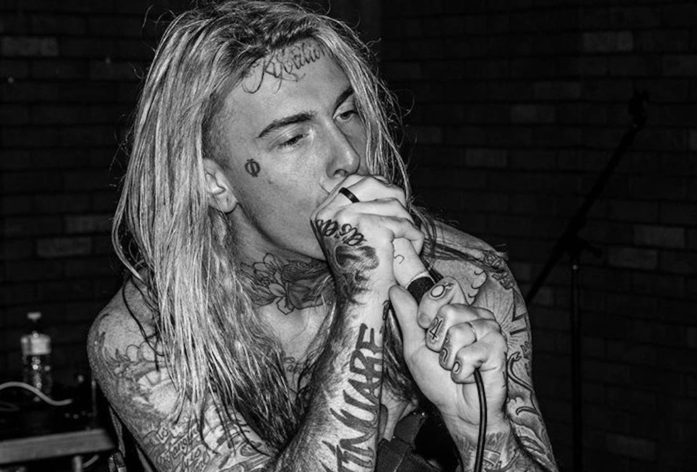 Ghostemane 桌布 壁紙 — 一位刺青長髮音樂家對著麥克風熱情歌唱，背景是磚牆，黑白風格。
