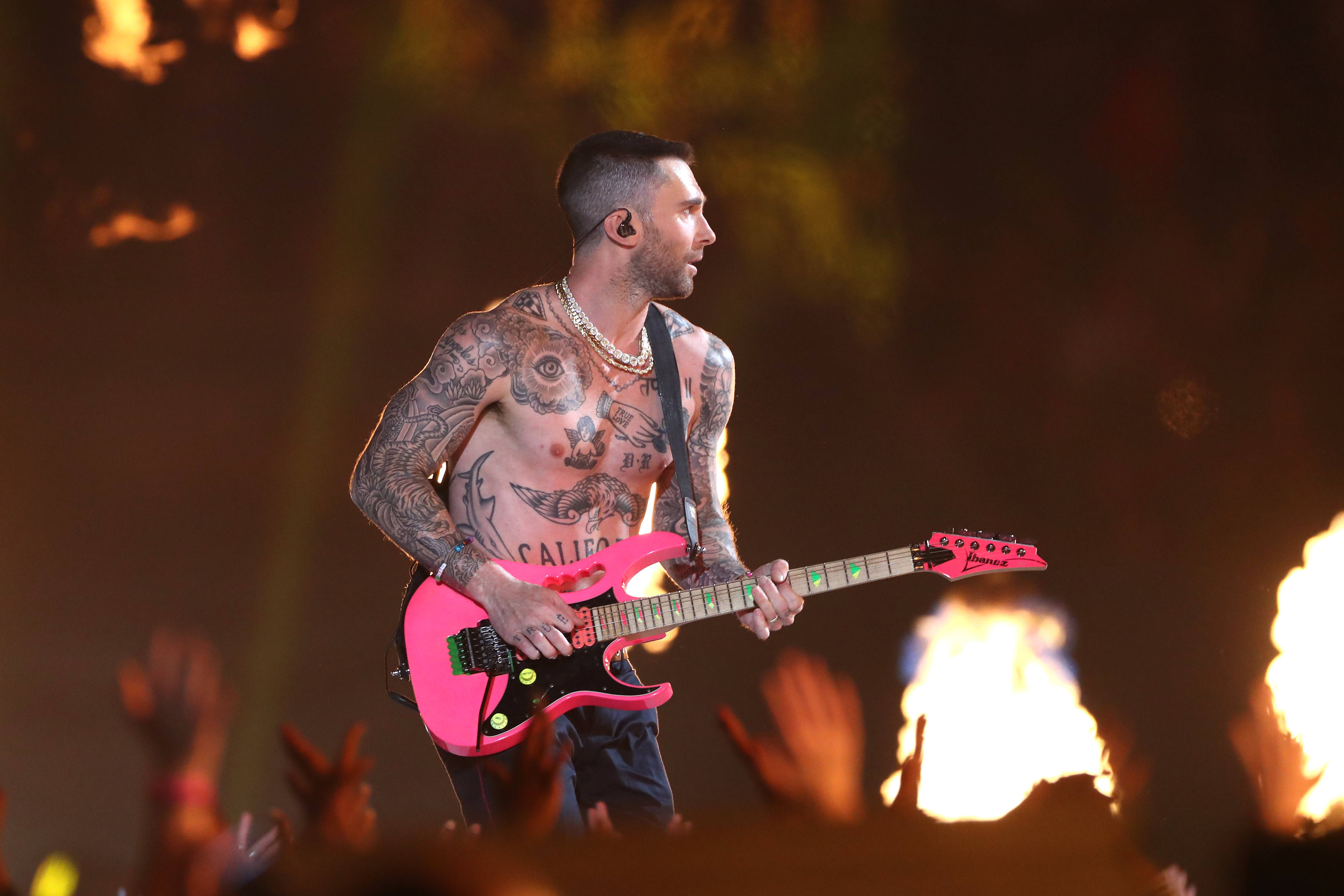 Adam Levine 桌布 壁紙 — 一位刺青音樂家在舞台上彈奏亮粉紅色電吉他，背後火焰爆發，粉絲在人群中舉起雙手。