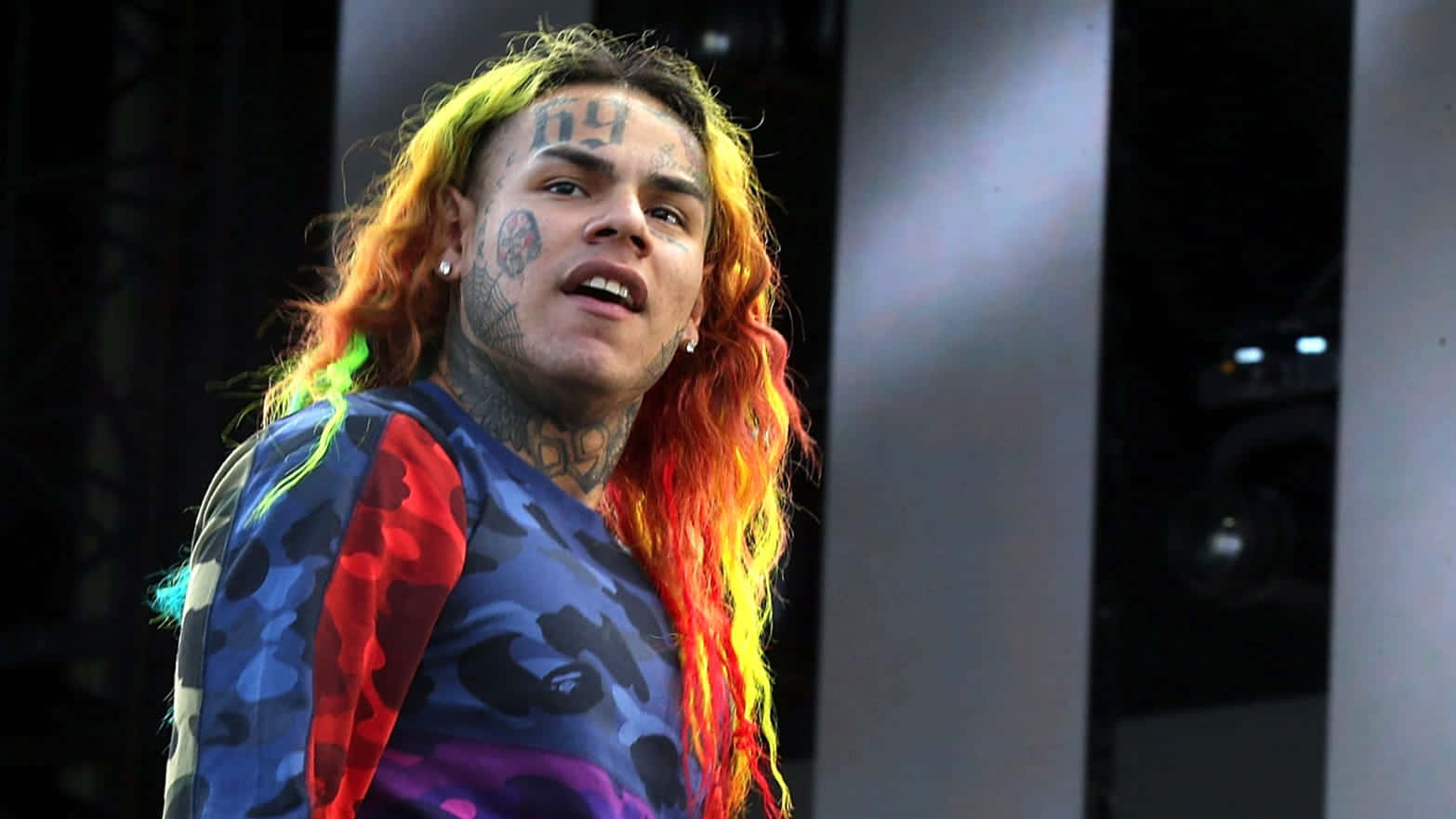 69 Rapper 桌布 壁紙 — 一位刺青音樂家擁有鮮豔的彩虹色頭髮，在明亮的燈光下於舞台上表演。
