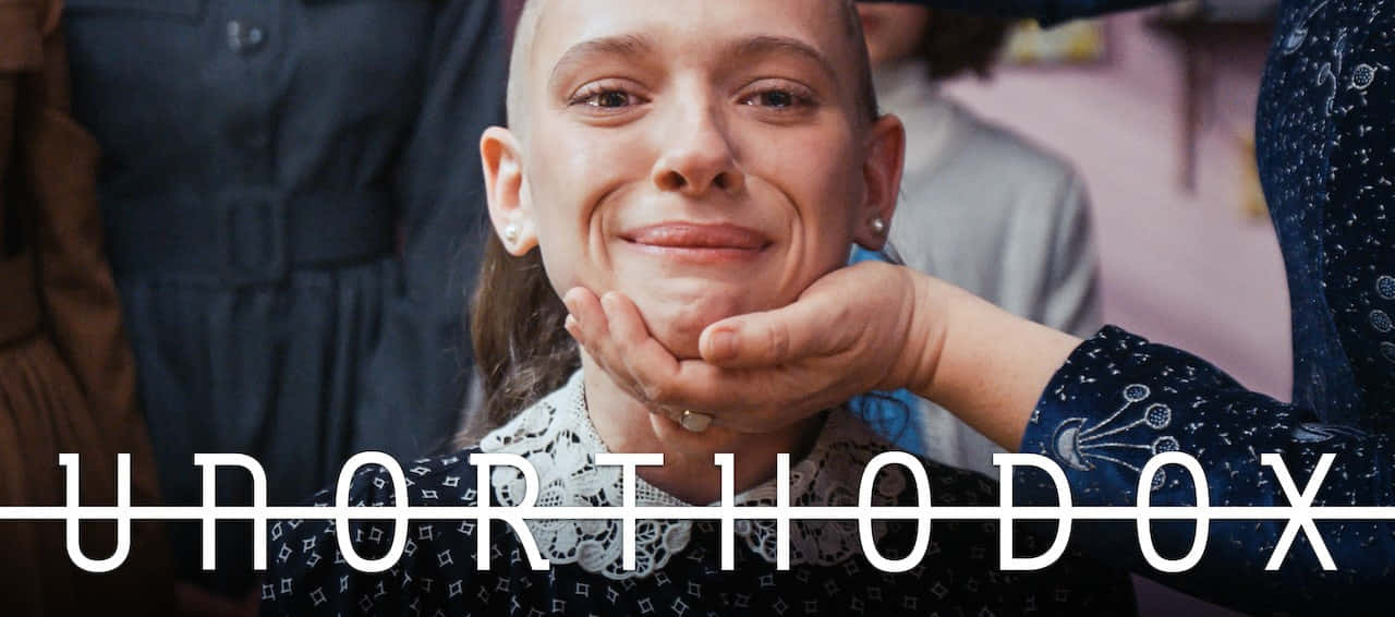 Unorthodox 桌布 壁紙 — 一位剃光頭的年輕女性微笑著，一隻手輕輕托住她的下巴，背景是柔和模糊的室內環境。