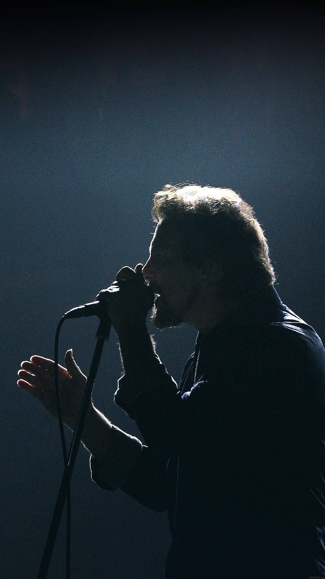 pearl jam 桌布 壁紙 — 一位剪影歌手在戲劇性的舞台燈光下，熱情地對著麥克風演唱。