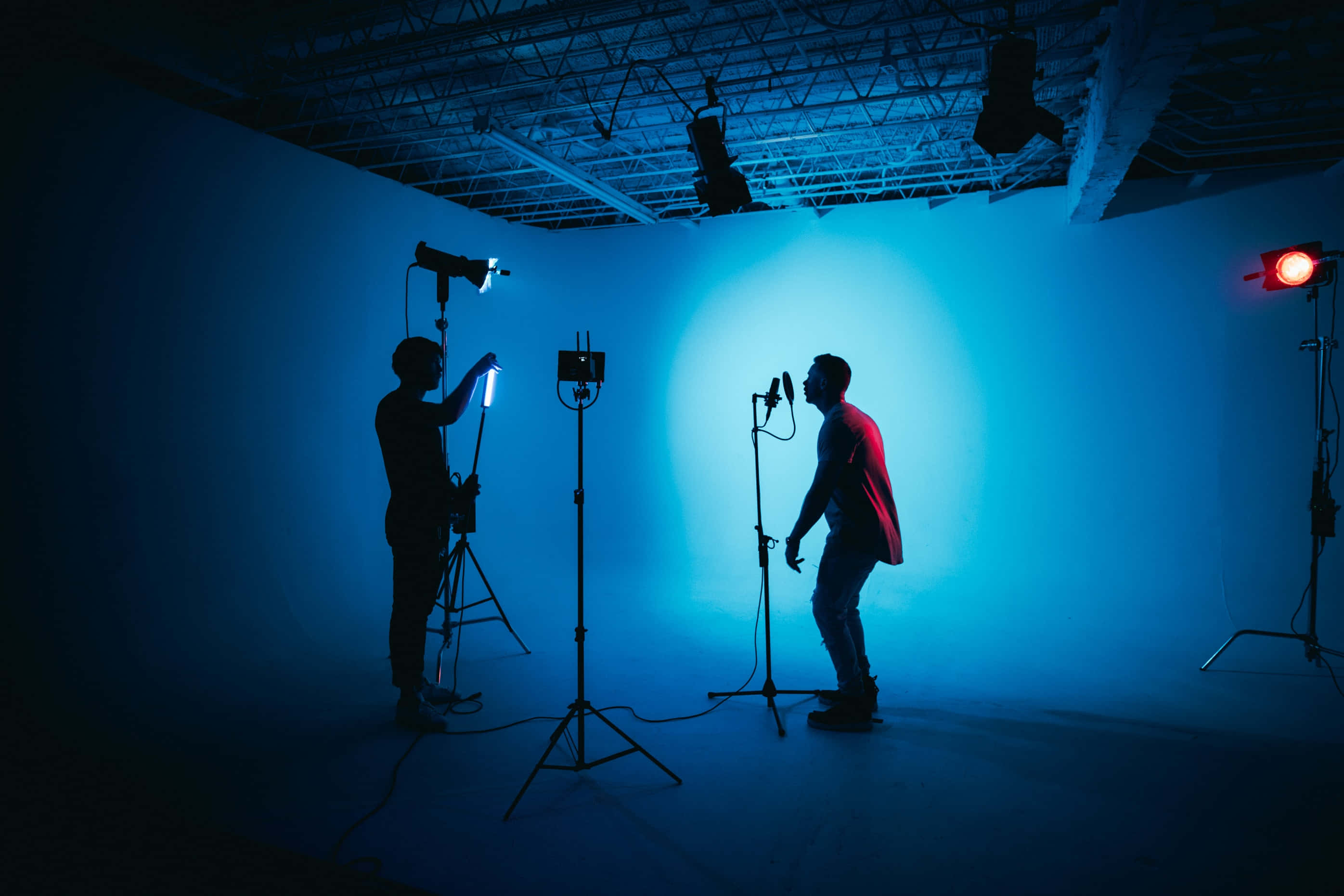 Photography Studio 桌布 壁紙 — 一位剪影音樂家在藍色聚光燈下對著麥克風表演，同時技術人員在錄音室調整燈光。