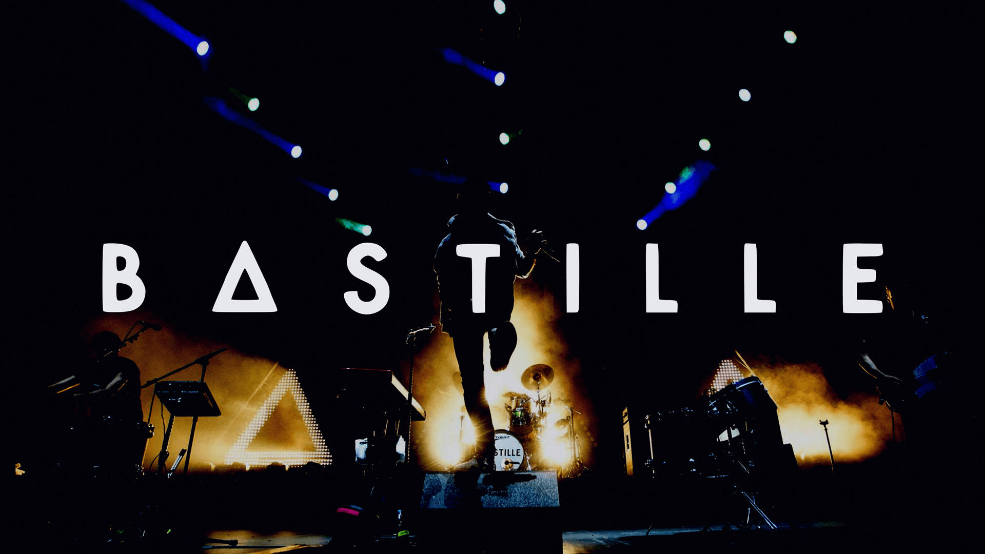 Bastille 桌布 壁紙 — 一位剪影音樂家在黑暗的舞台上表演，舞台被火橙色和電光藍色燈光籠罩，樂隊名稱 Bastille 以粗體白色字母呈現。