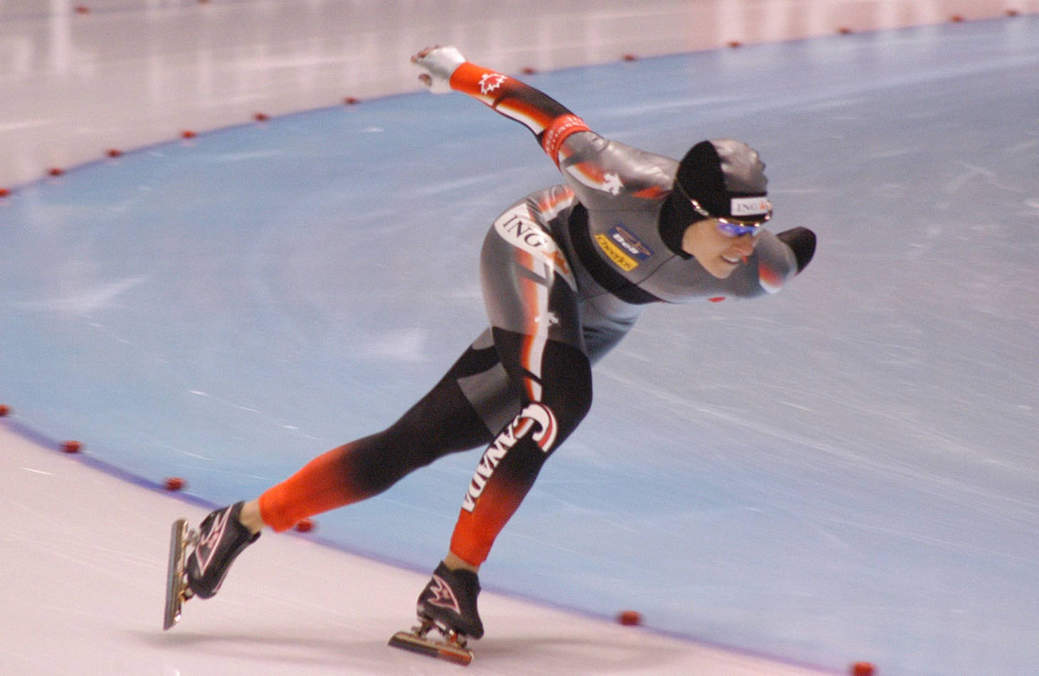 Olympics 桌布 壁紙 — 一位加拿大速度滑冰選手在室內溜冰場上穿著流線型空氣動力學服裝傾身過彎。