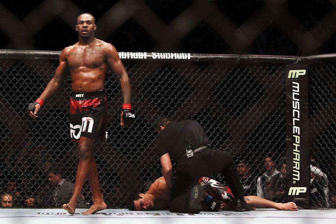 UFC 桌布 壁紙 — 一位勝利的MMA拳手在八角籠中威風凜凜地站立，裁判正在檢查地上的對手。