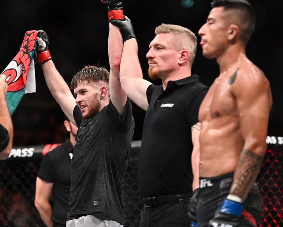 MMA 桌布 壁紙 — 一位勝利的MMA拳手在八角籠中慶祝，裁判舉起他的手臂，肩上披著旗幟。